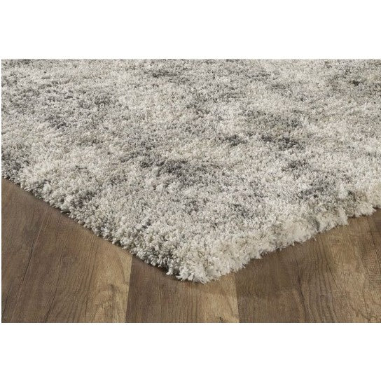 Corner of a textured grey and white rug on wood flooring.