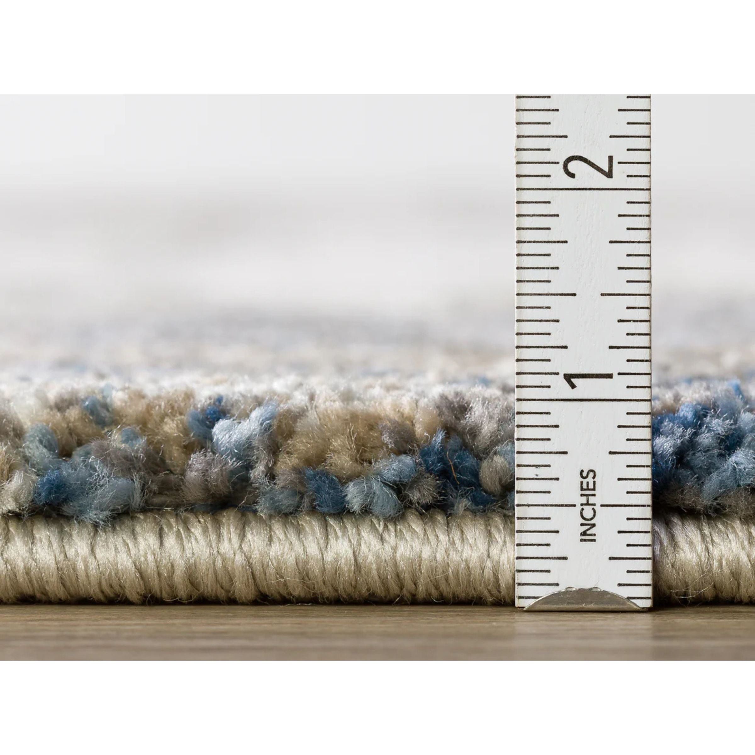 Close-up of a rug edge with a ruler showing the height is just under 1 inch.