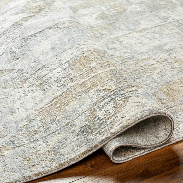 Beige and gray area rug with a textured, abstract pattern shown rolled on hardwood floor.