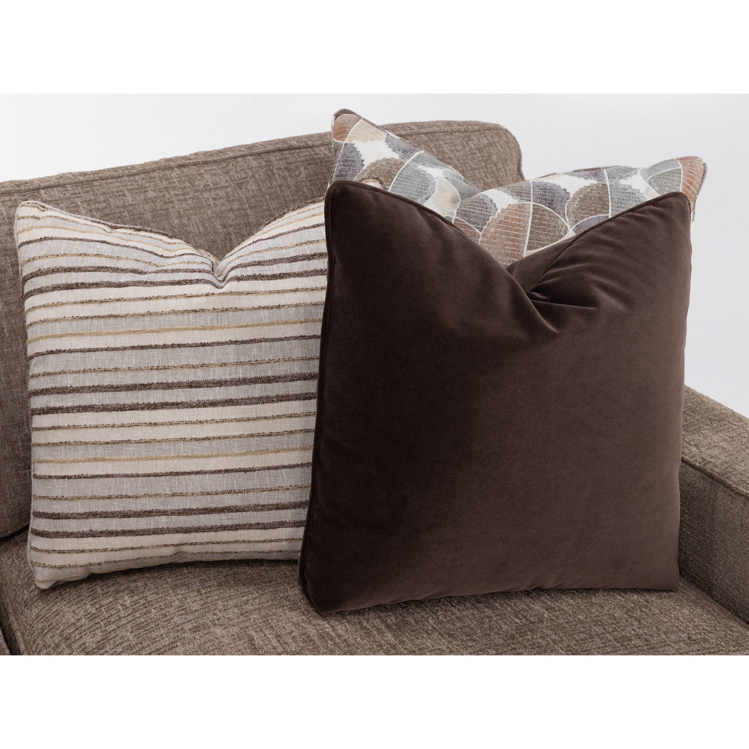 Two decorative throw pillows on a brown sofa, one striped and one solid dark brown.