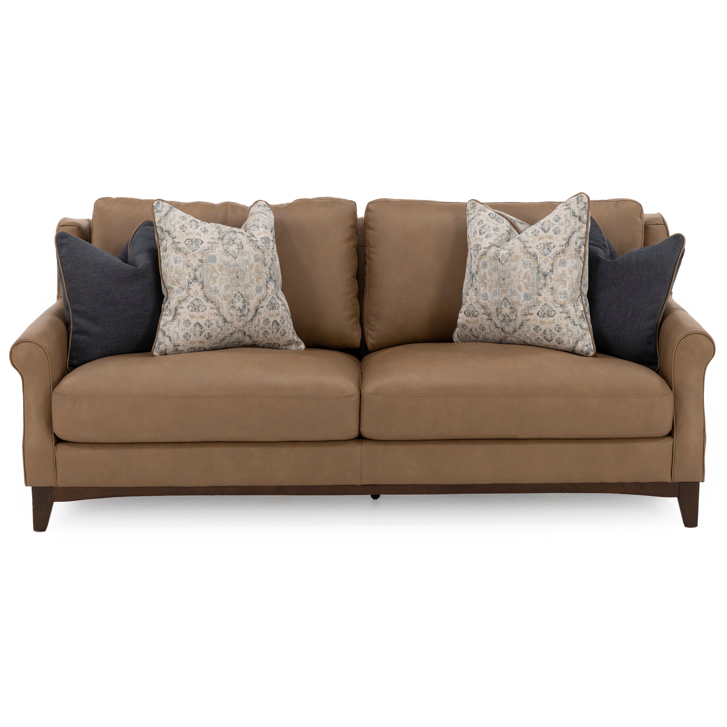 Brown leather sofa with four decorative pillows, two patterned and two solid.