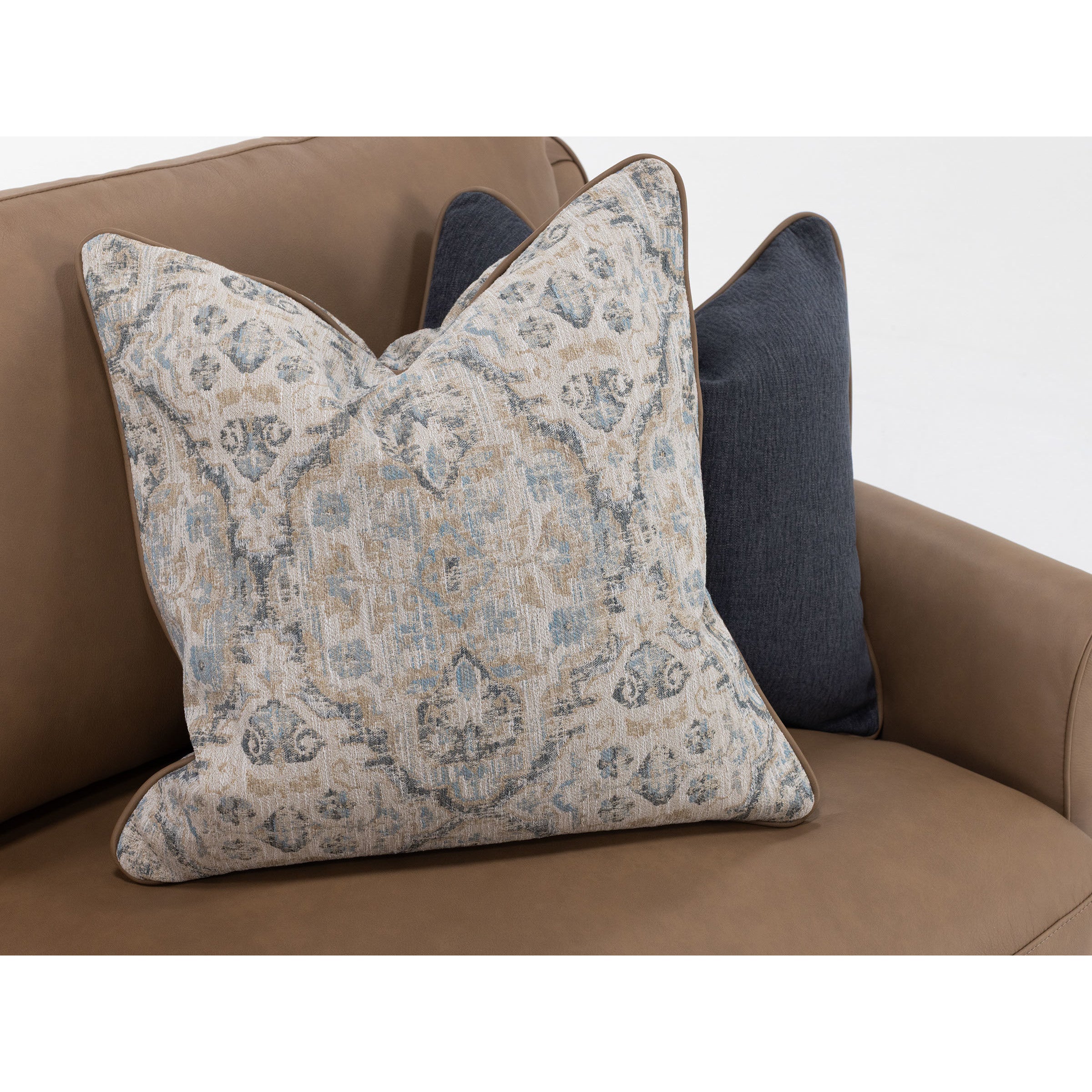 Two decorative pillows on a tan sofa, one with a beige and blue pattern, one solid dark gray.