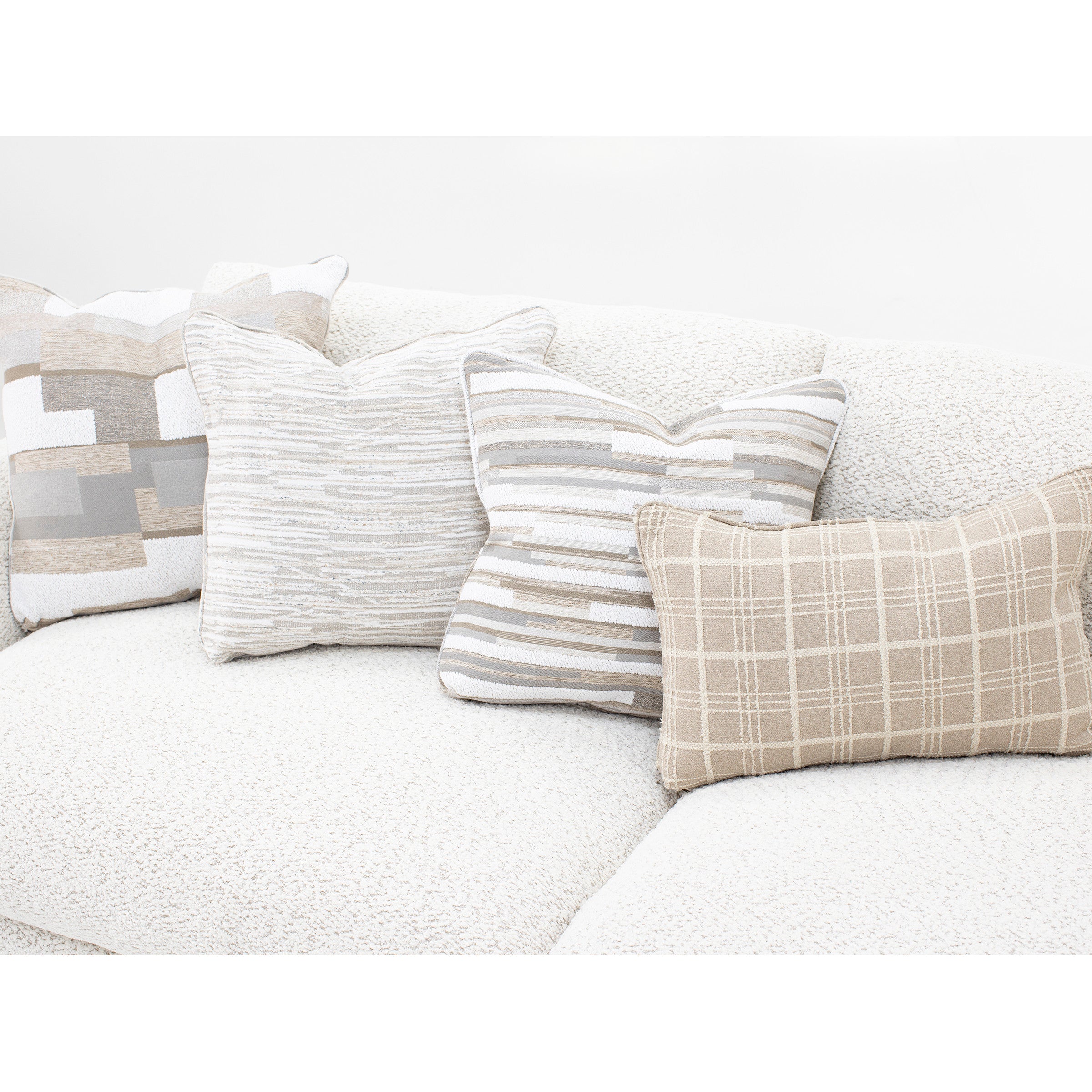 Four neutral decorative pillows arranged on a light textured sofa.