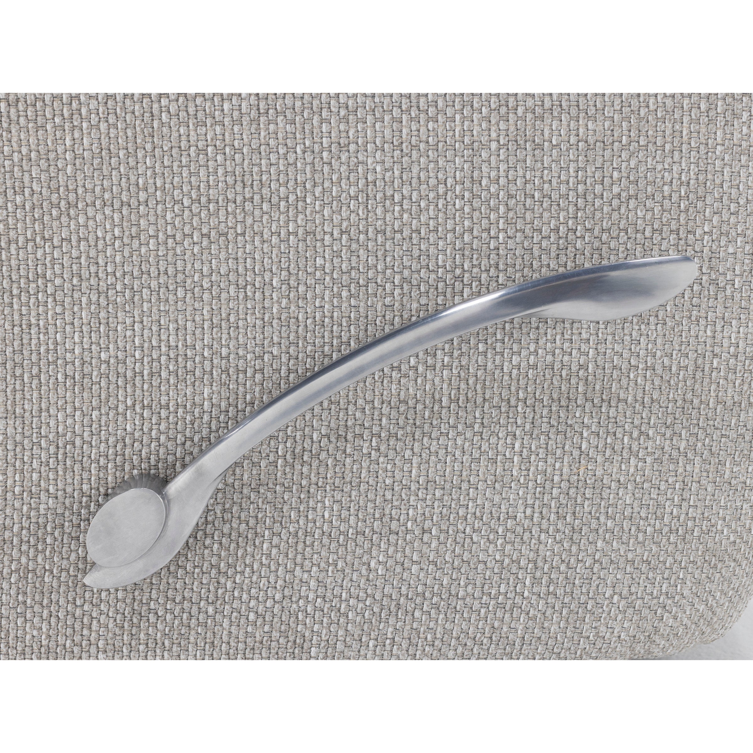 Curved metal utensil with a flat end on textured fabric background.