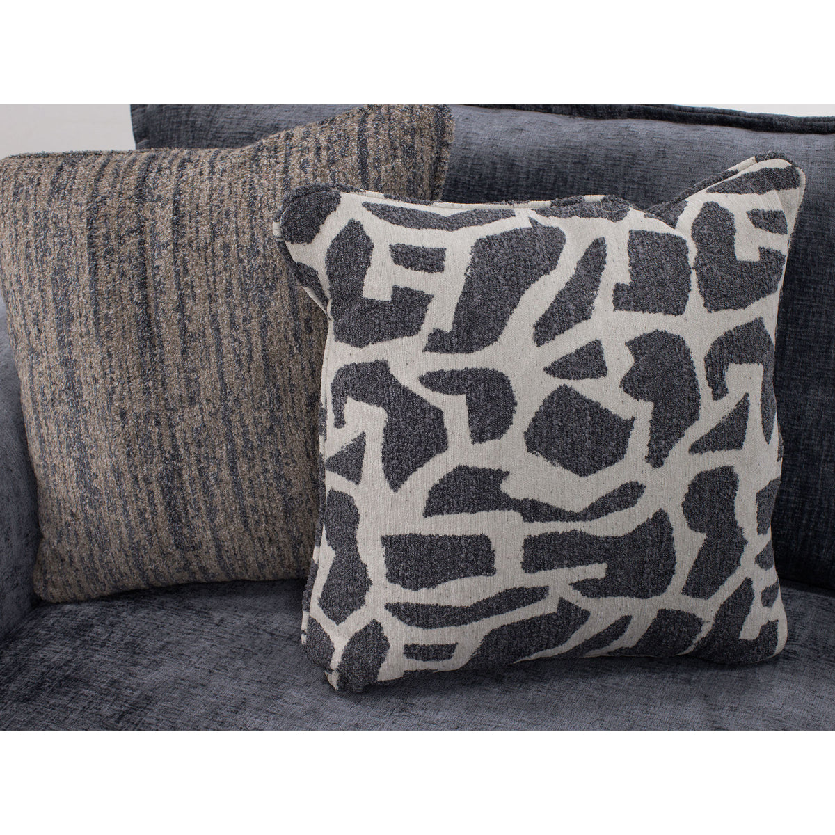 Two decorative pillows on a grey sofa, one with a geometric pattern, one with textured stripes.