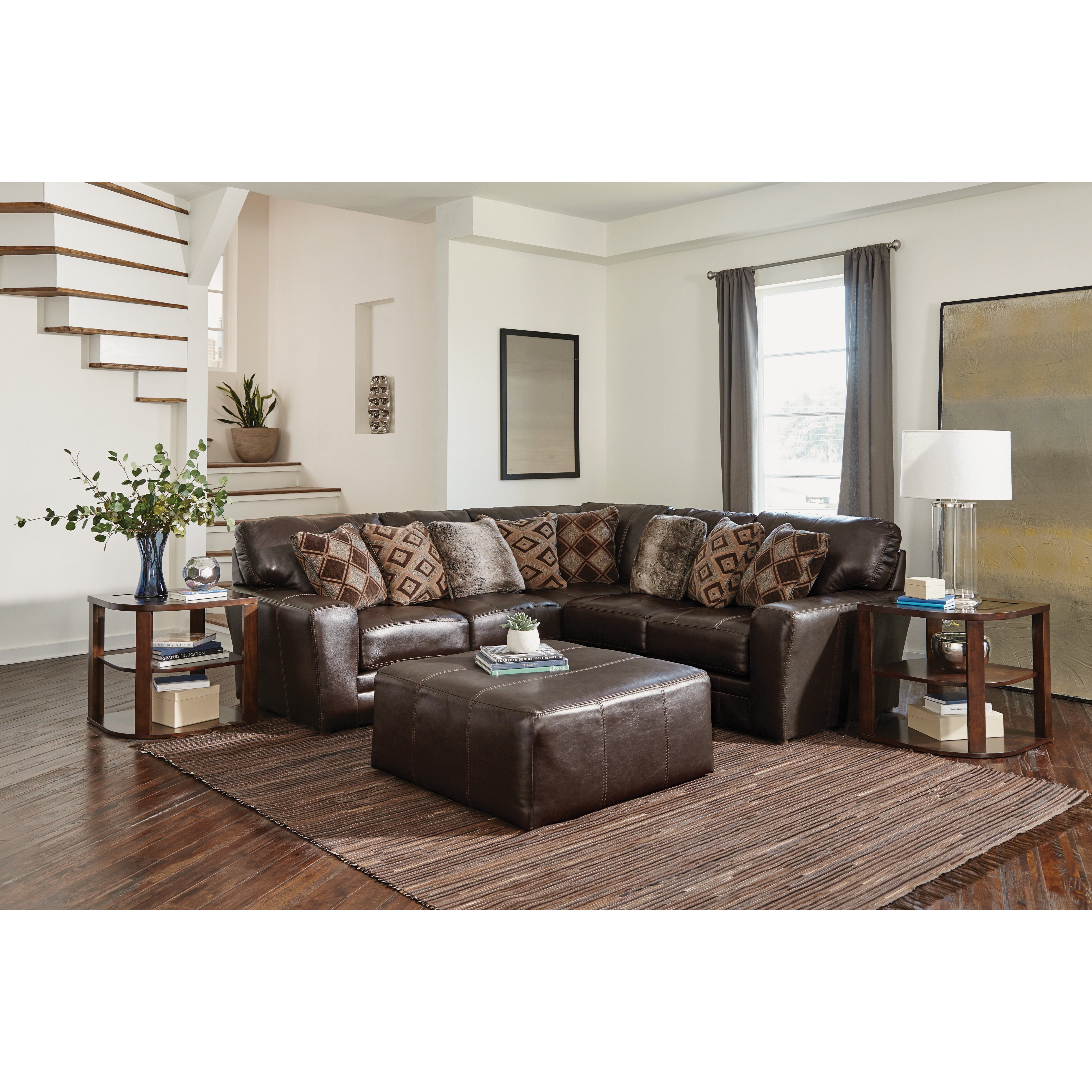 Modern living room with a dark brown leather sectional, patterned pillows, and a large ottoman.