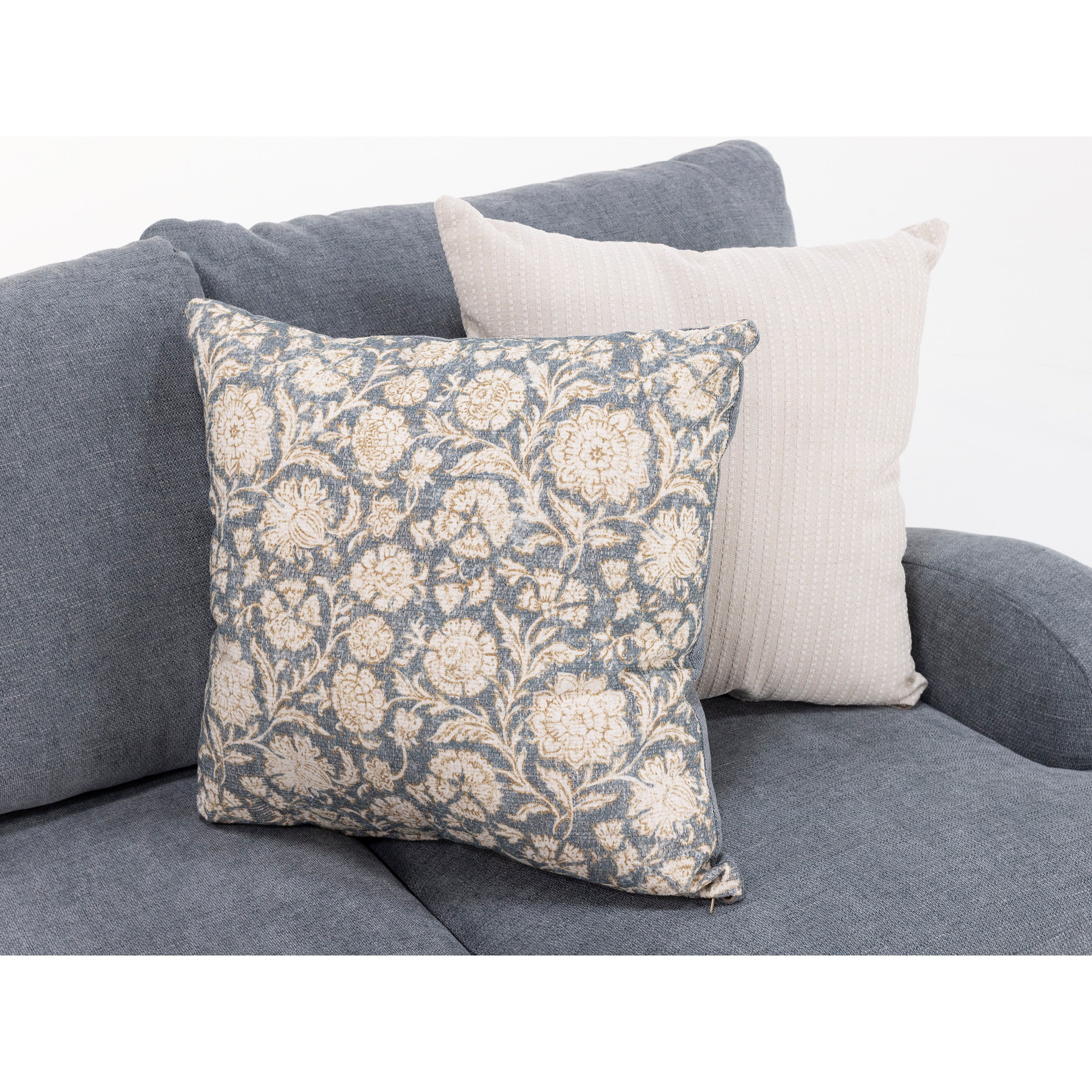 Two decorative throw pillows on a gray fabric sofa, one with a floral pattern, one solid light color.