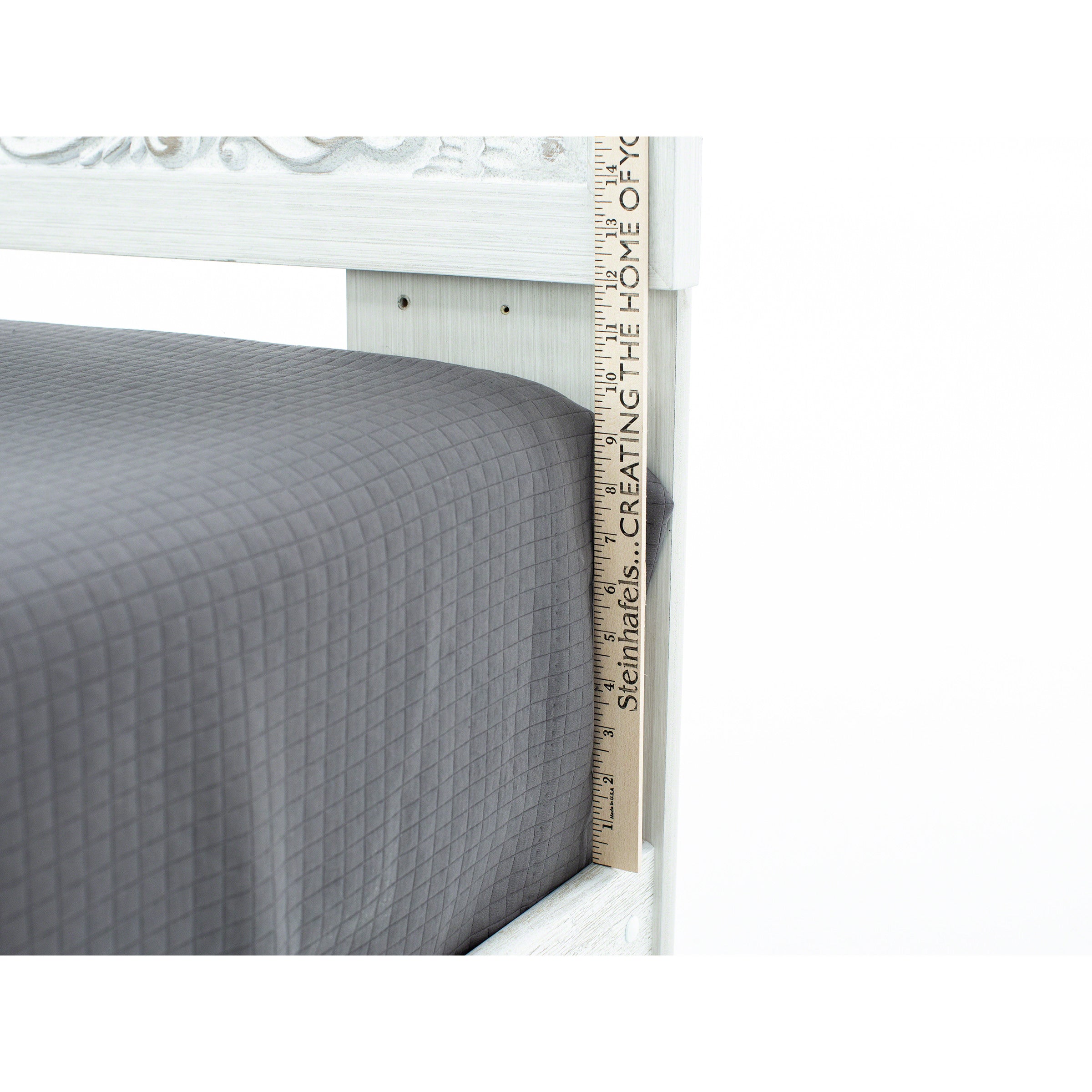 Ruler measuring the height of a gray mattress on a white bed frame.