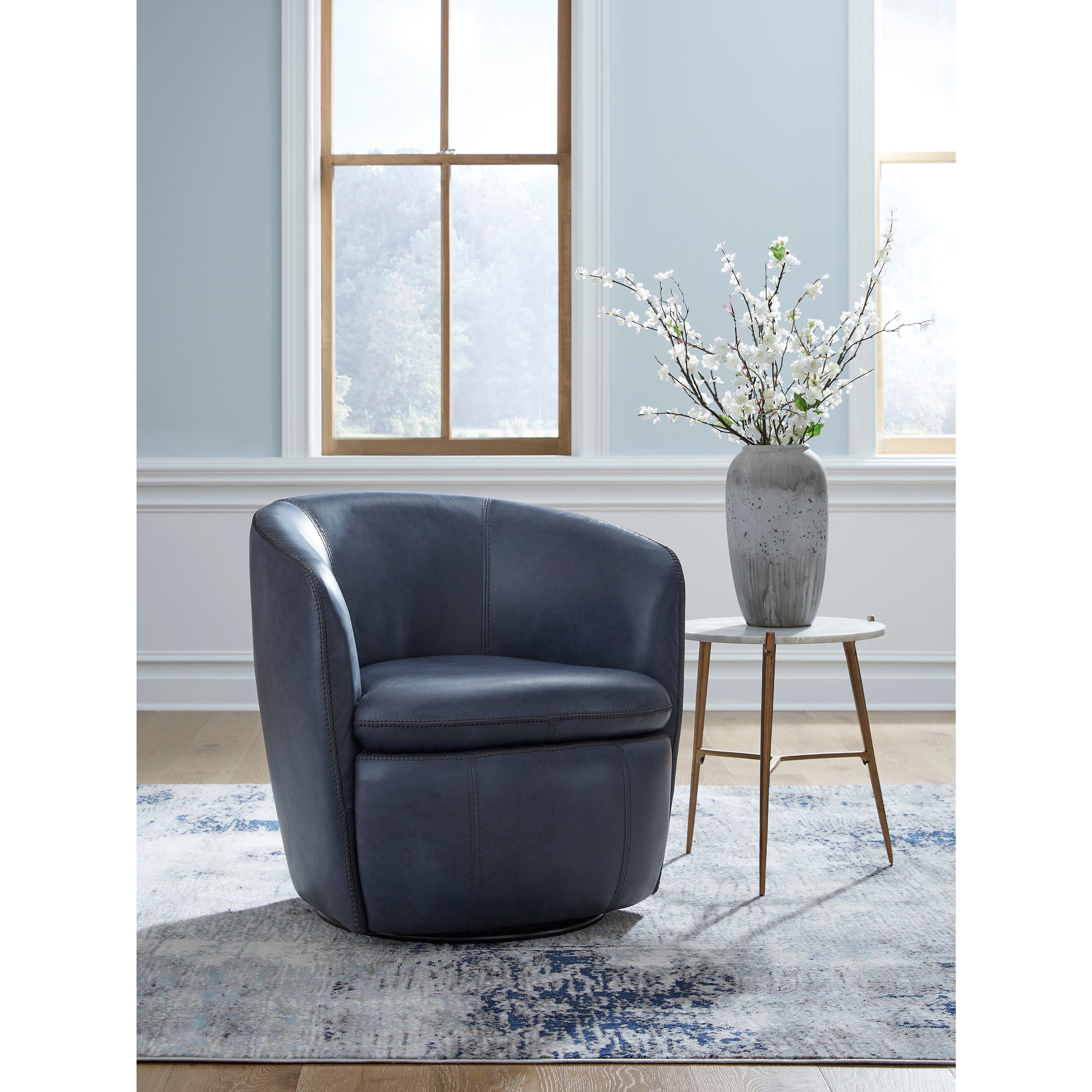 Blue leather accent chair beside a vase of white flowers on a small table in a bright room.