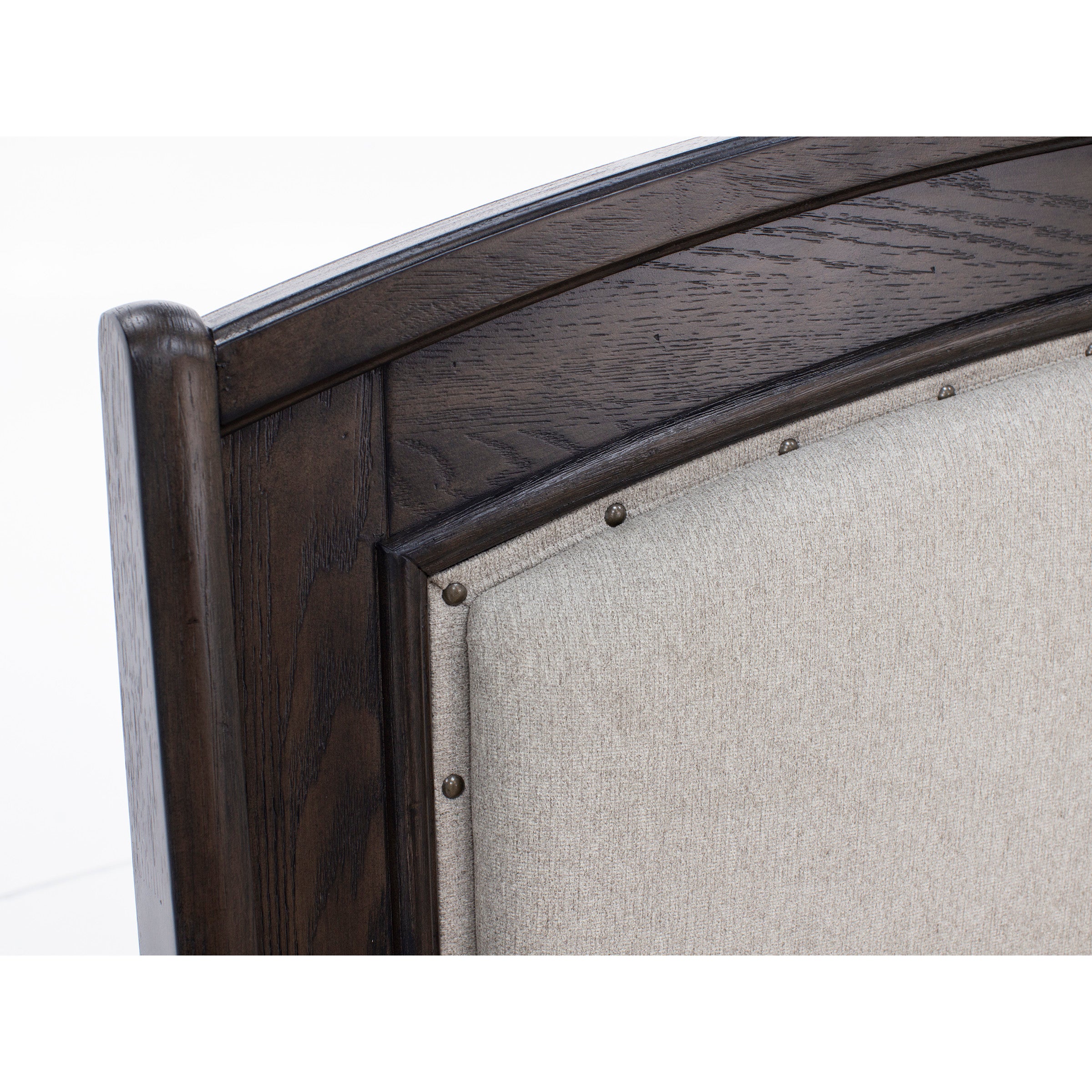 Close-up of a dark wood bed frame with beige upholstered panel and nailhead trim.
