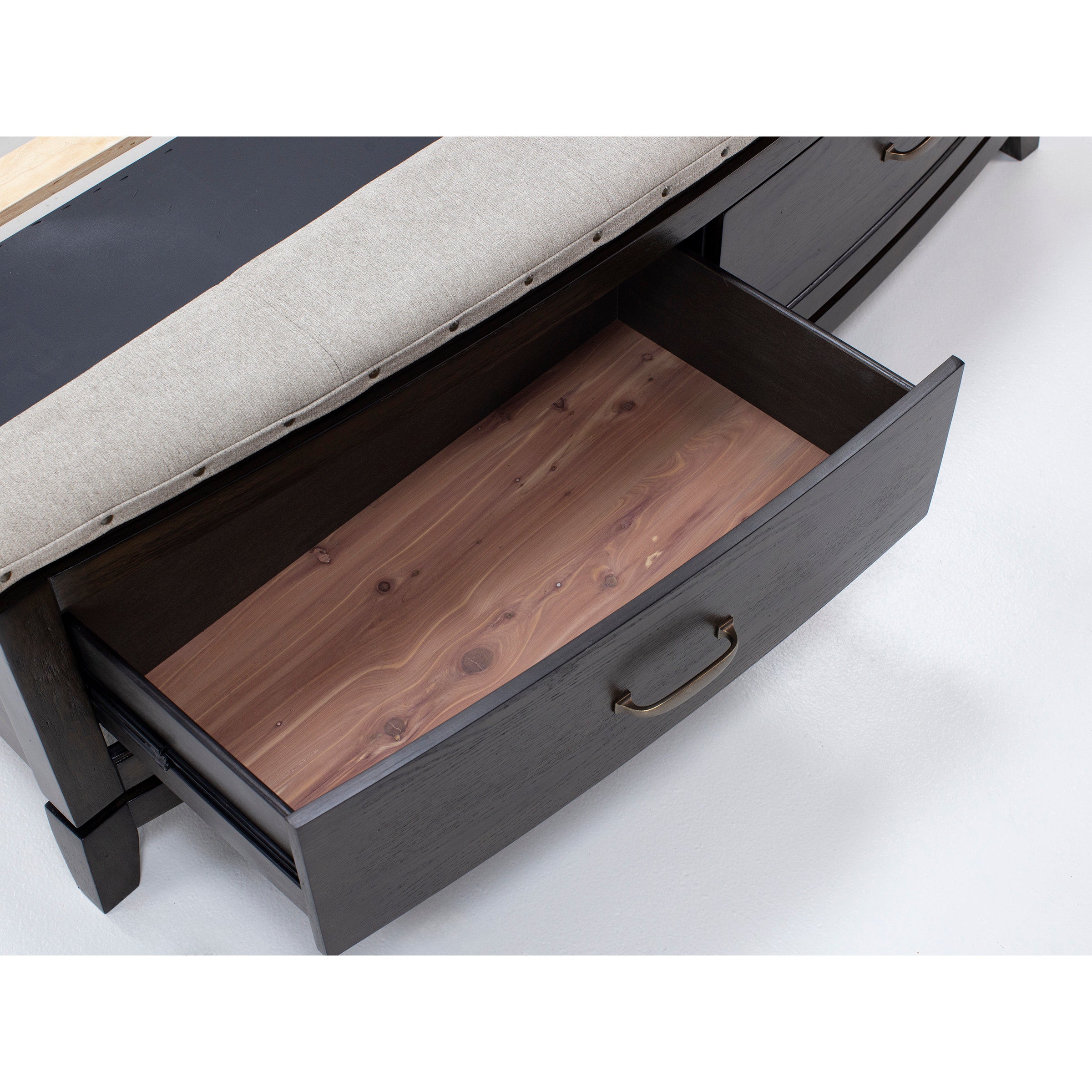 Open wooden storage drawer with metal handle under upholstered bench.