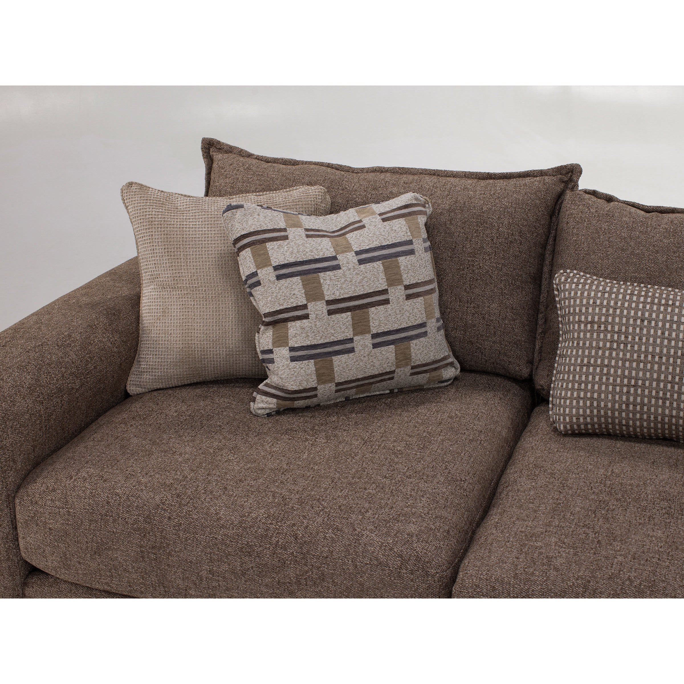 Close-up of a brown fabric sofa with three decorative pillows in beige and geometric patterns.