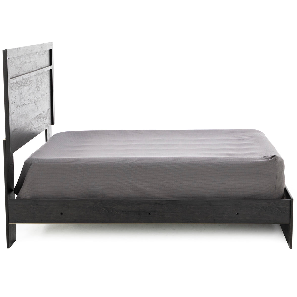 Side view of a modern bed with a gray sheet and tall wooden headboard.