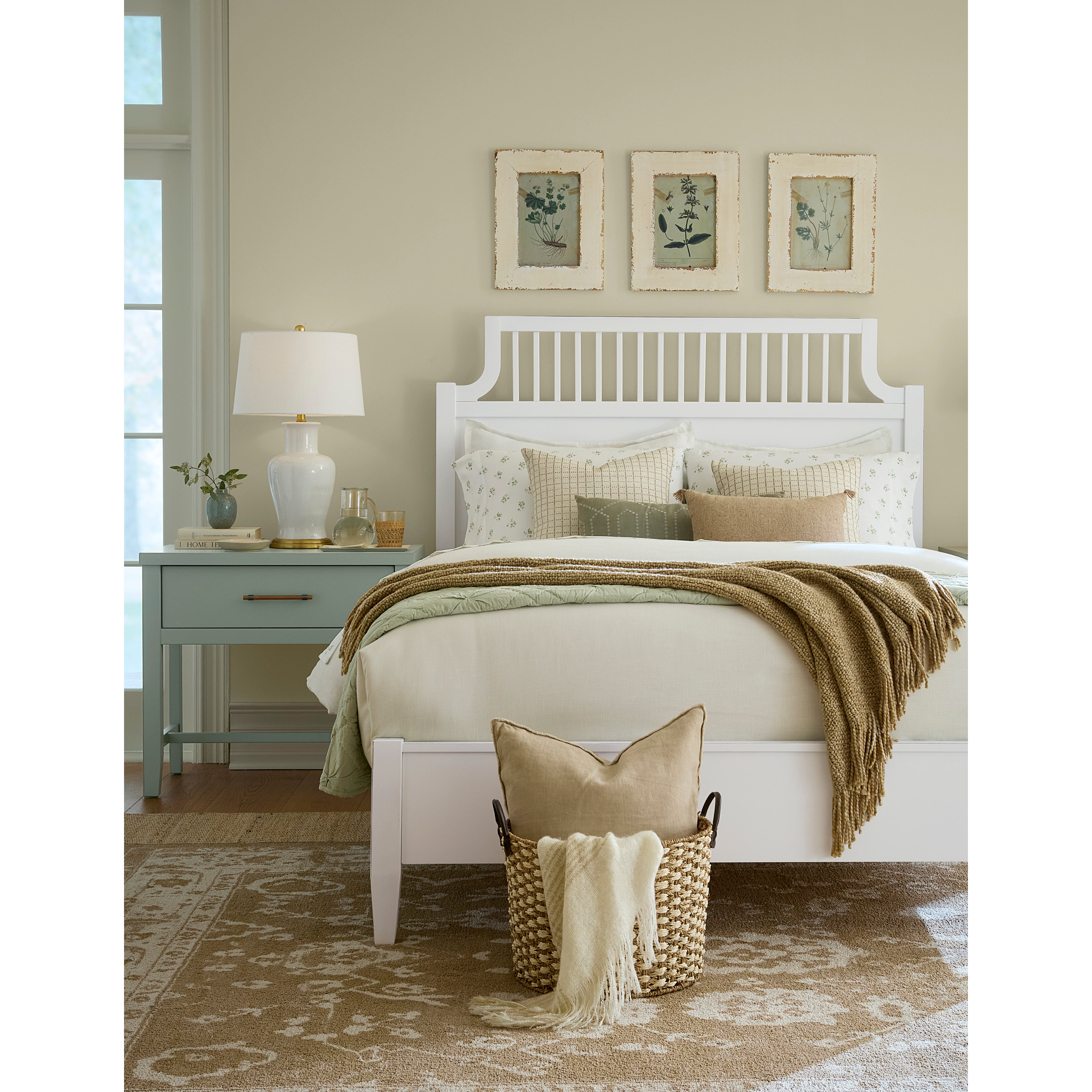 Bedroom with white bed, beige bedding, cozy throw, and three botanical prints above the headboard.