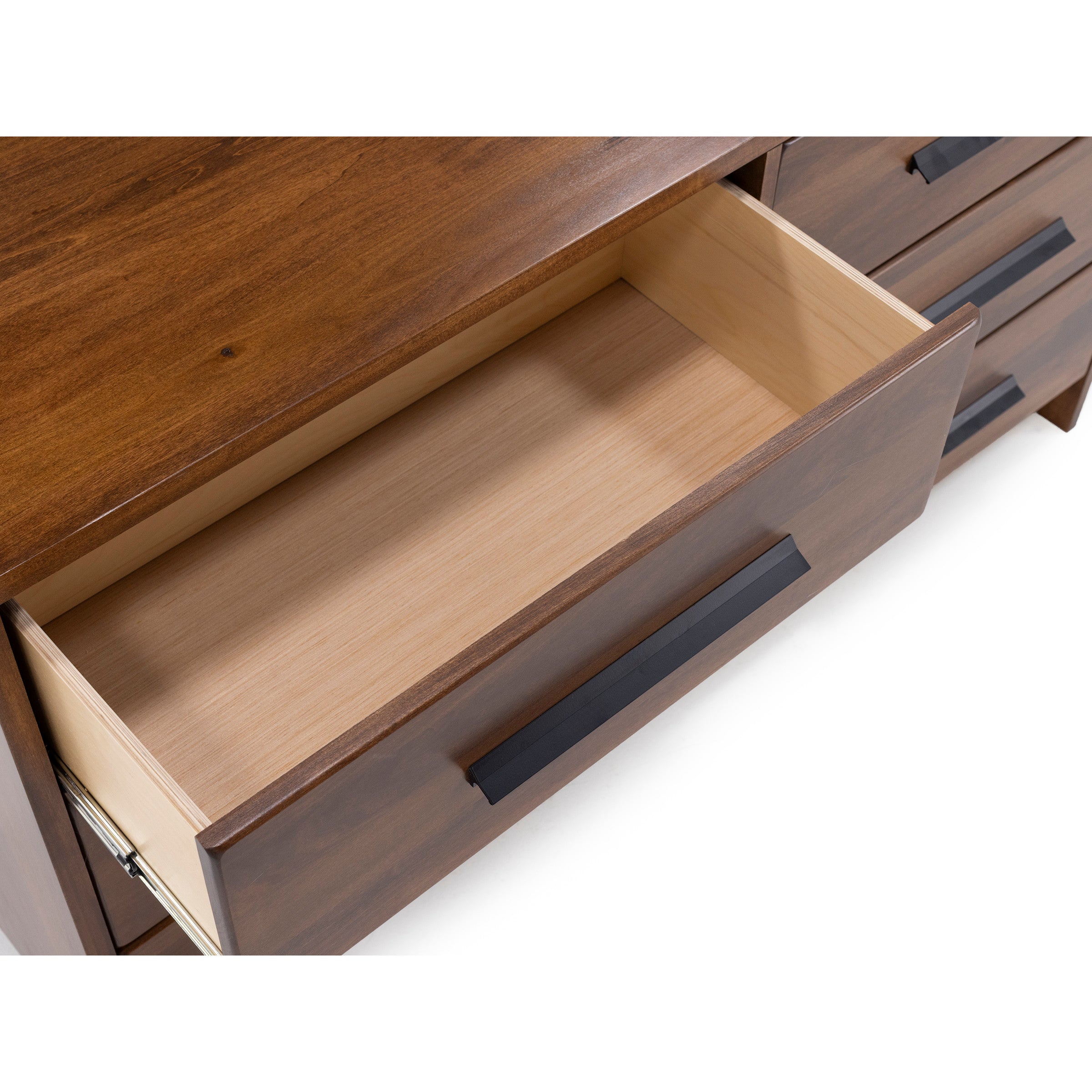 Open top drawer of a wooden dresser with modern black handles.