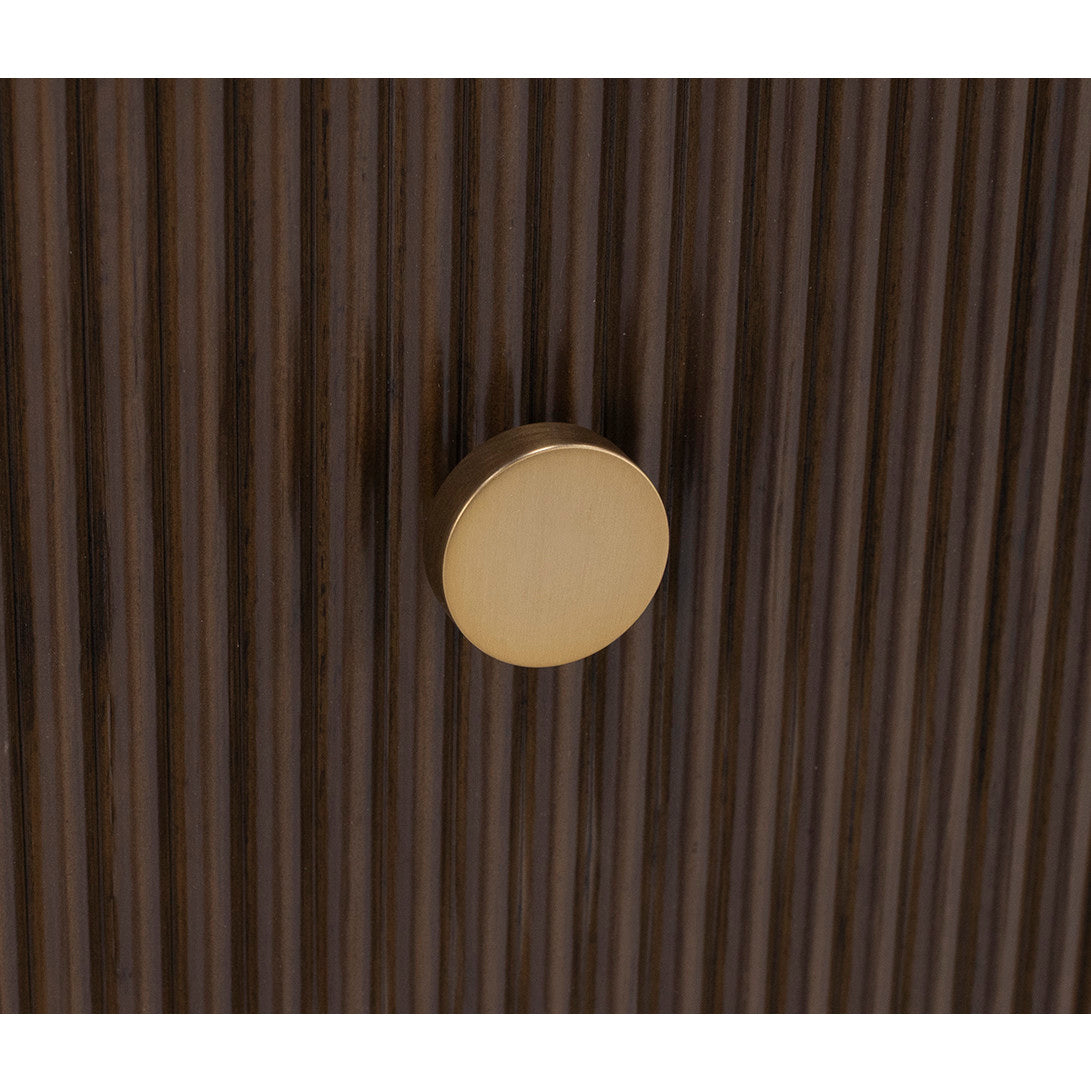 Round brass knob on dark wood cabinet with vertical ridges.