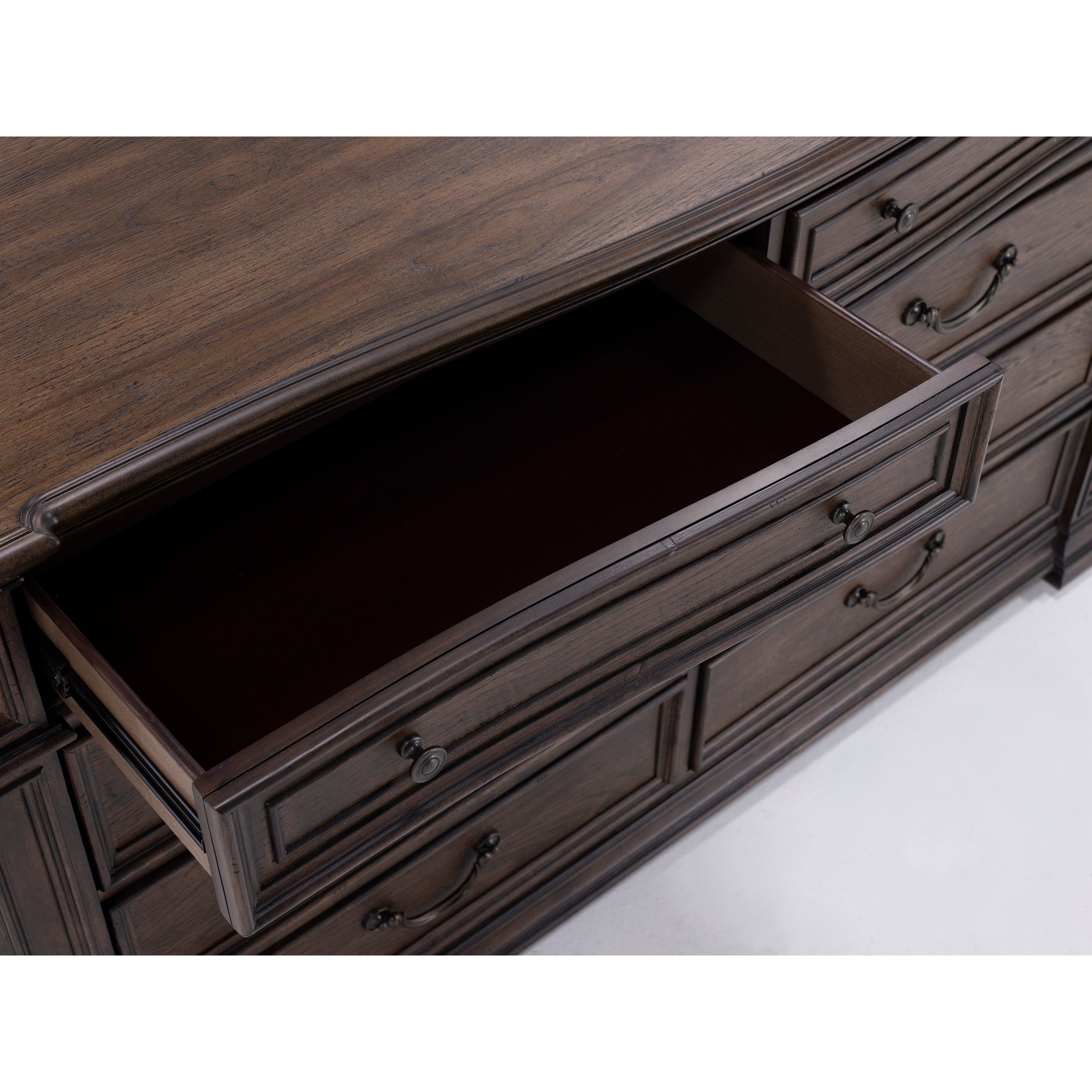 Open top drawer of dark wood dresser with classic metal handles.