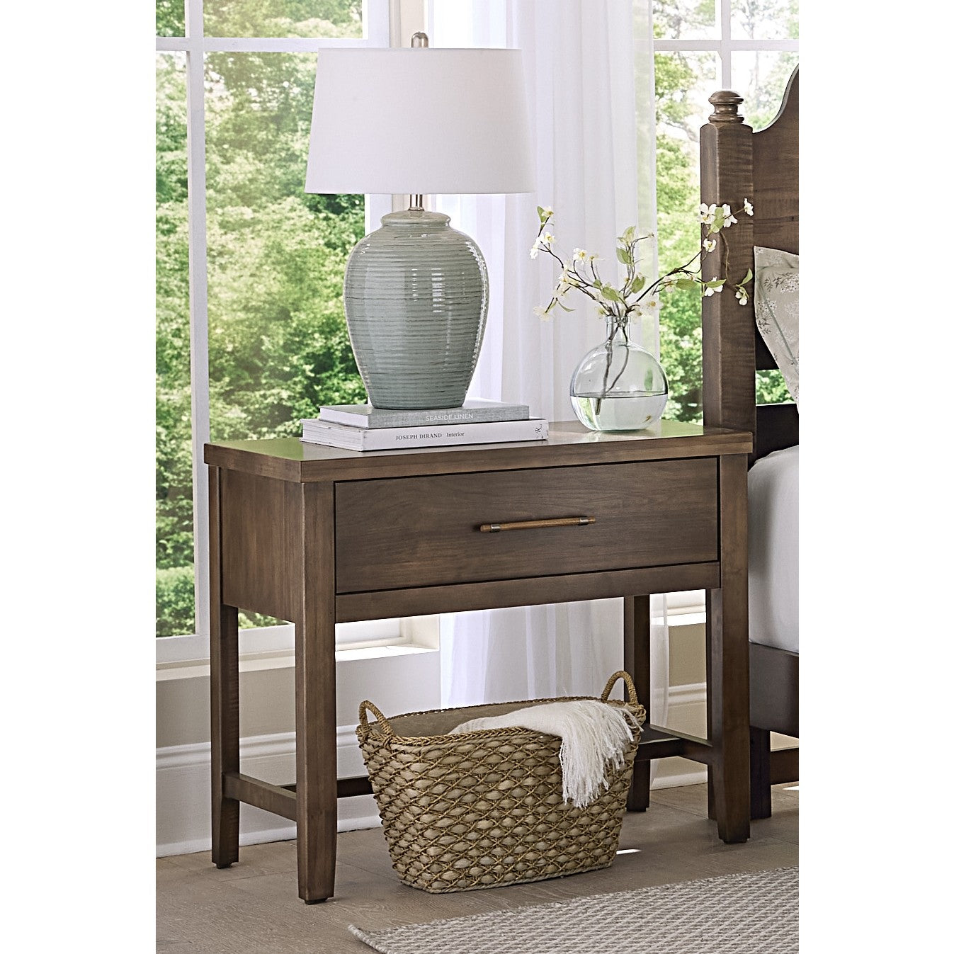 Wood nightstand with drawer, table lamp, books, and a basket below.