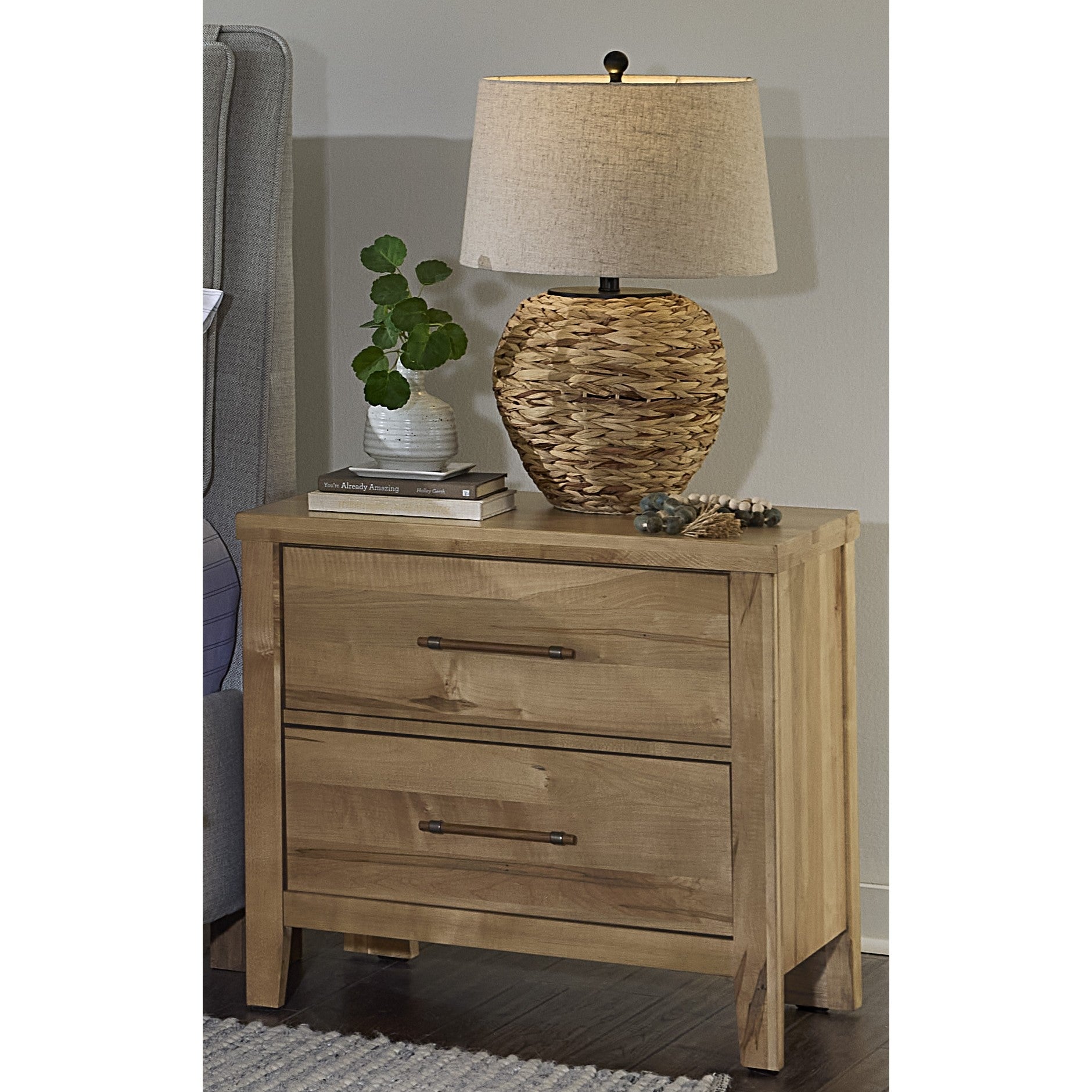 Natural wood nightstand with two drawers, lamp, plant, and books on top.