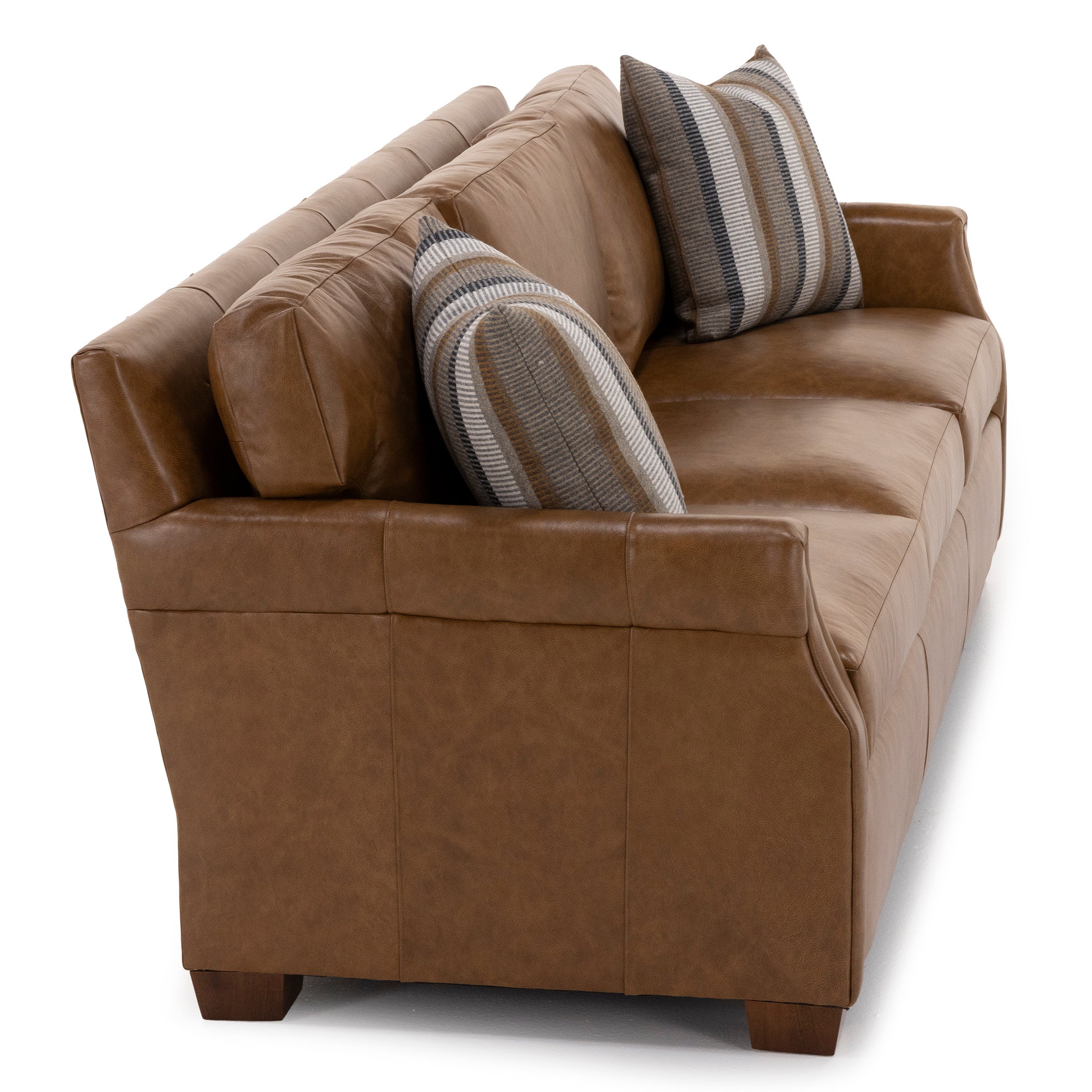 Angled view of a brown leather sofa with two striped accent pillows.