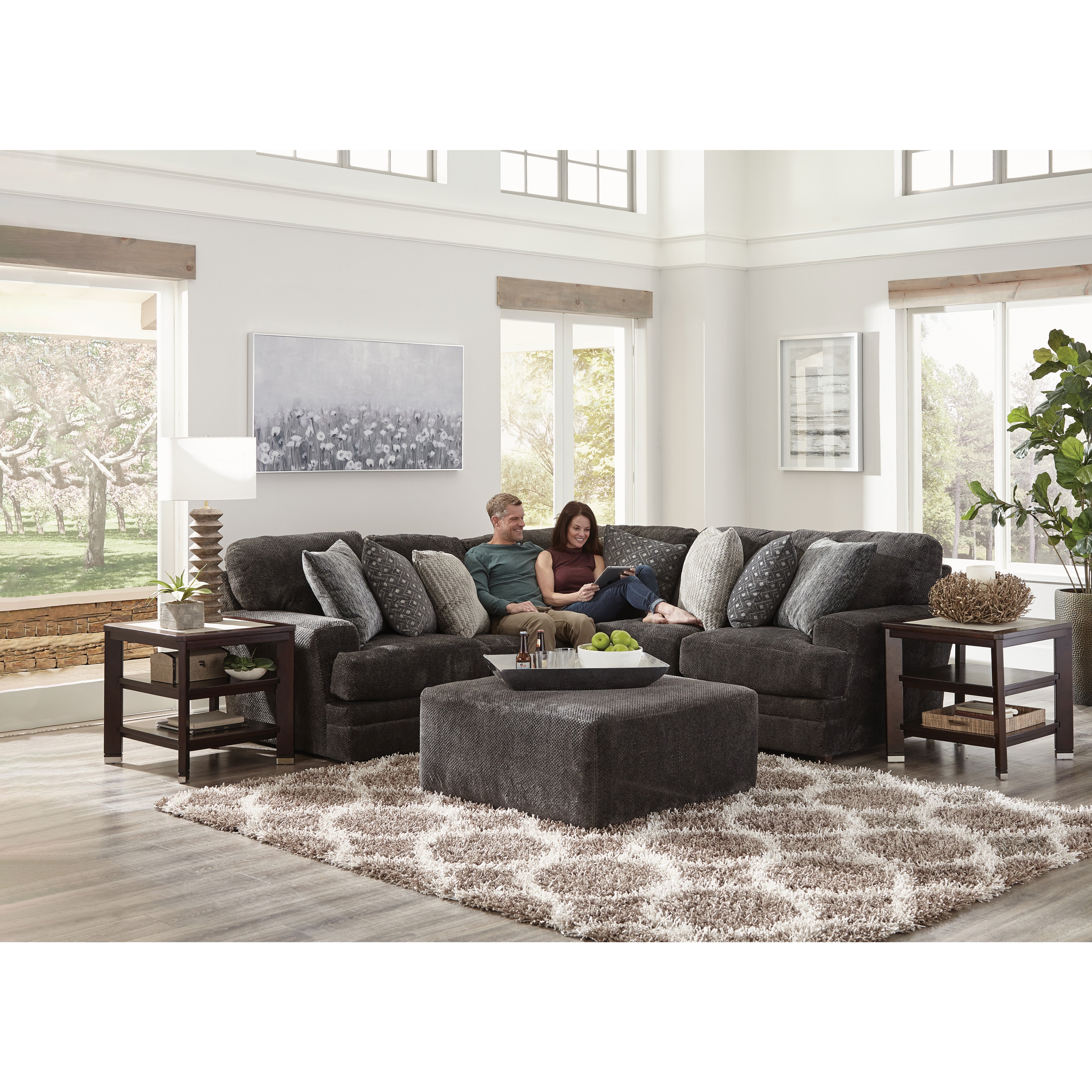 Couple relaxing on a dark sectional sofa in a bright living room with large windows.