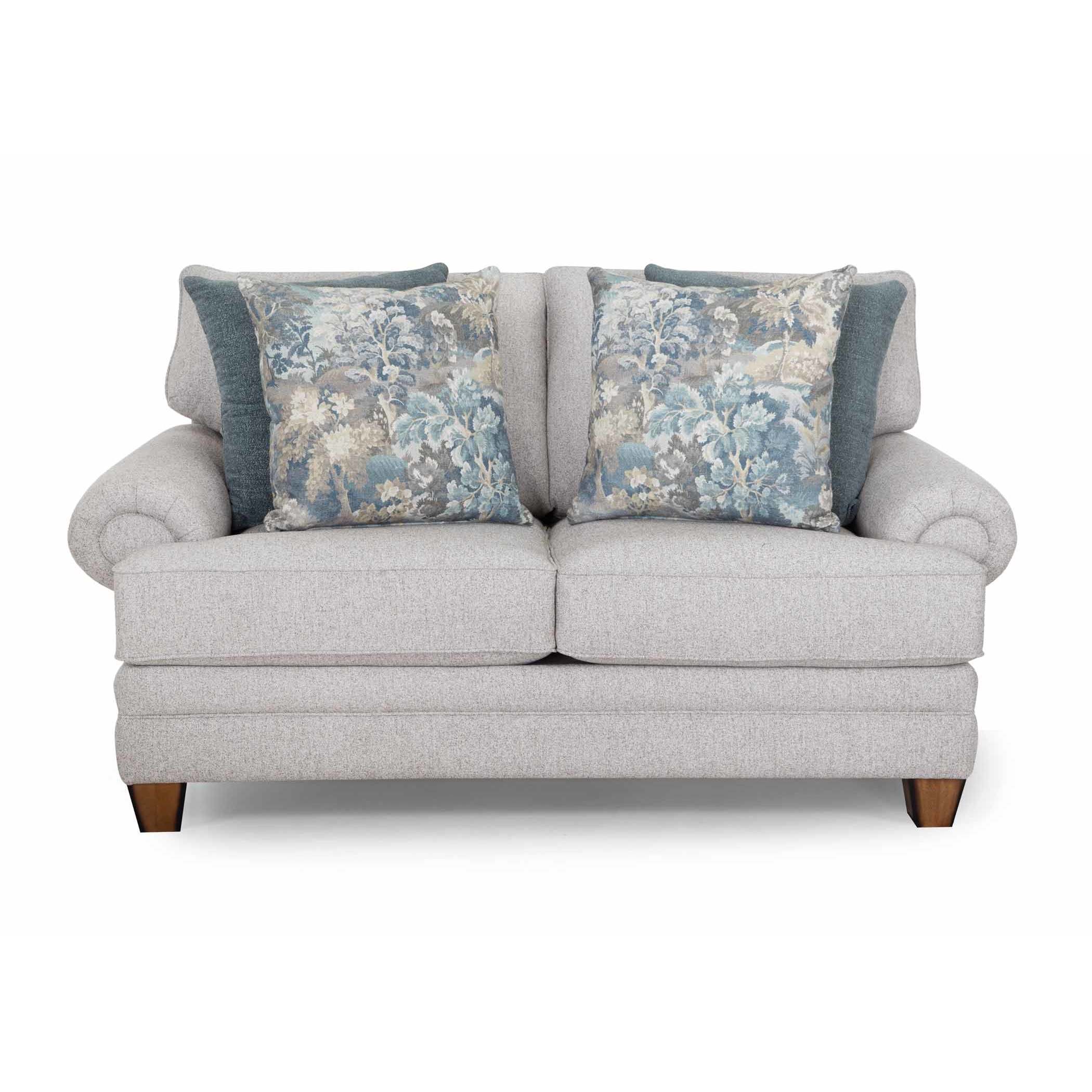 Light gray loveseat with rolled arms and two blue floral accent pillows.