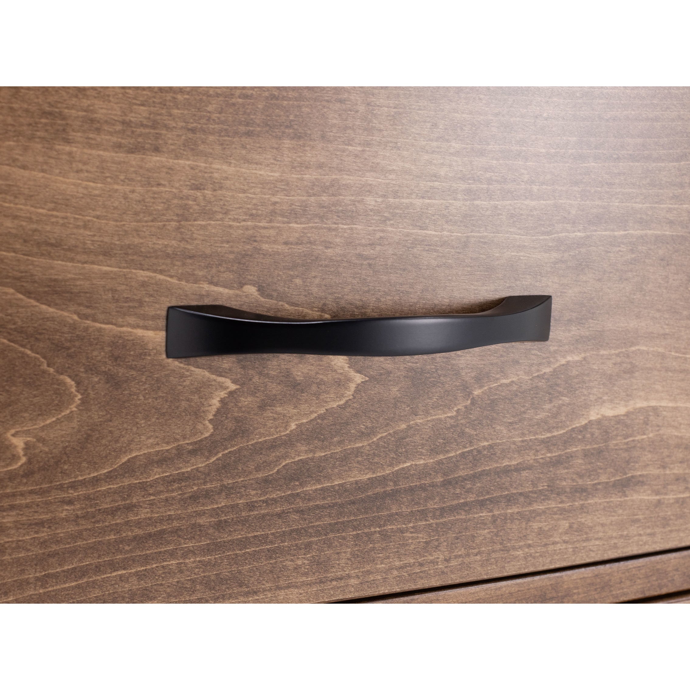 Black drawer handle on light wood drawer front.