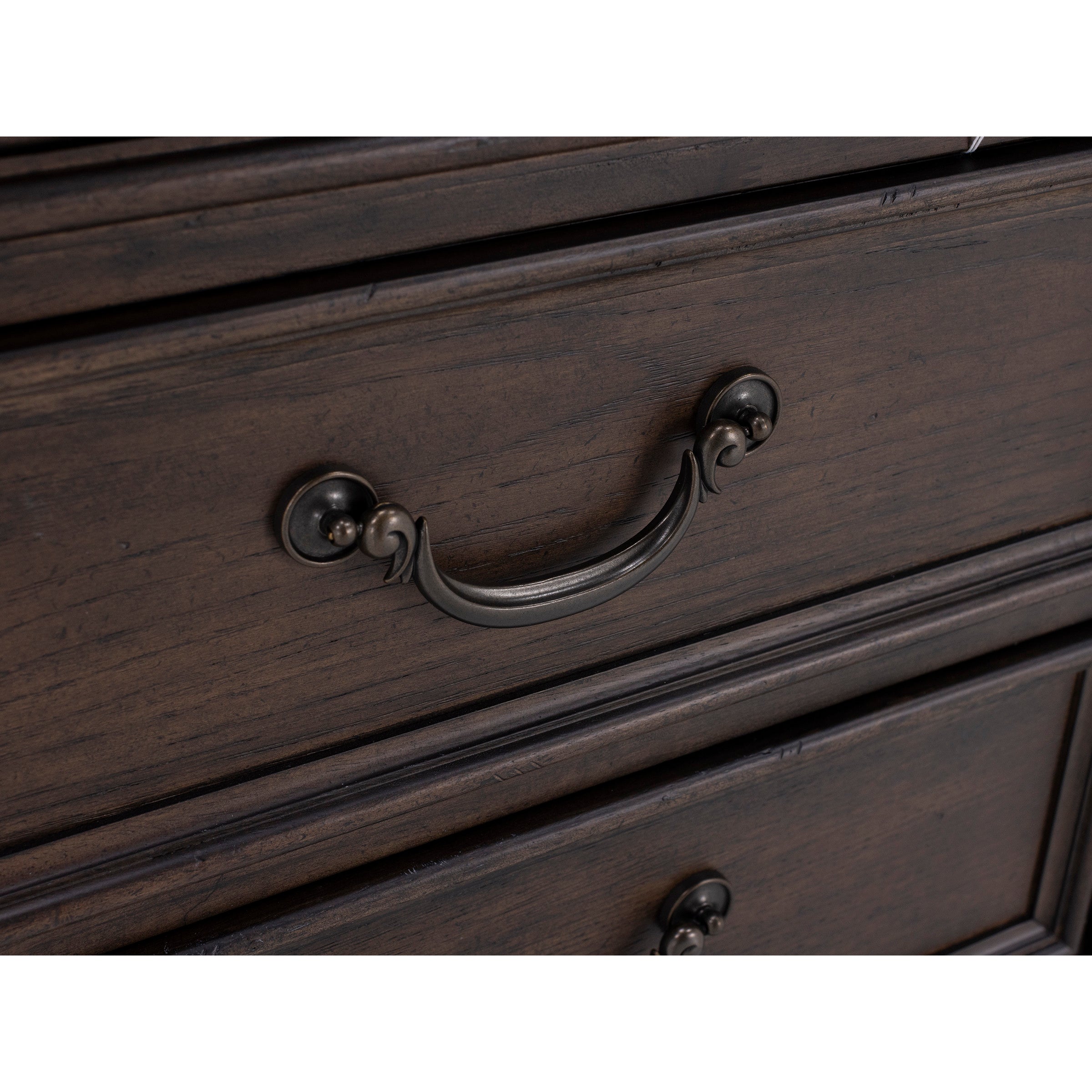 Close-up of an ornate metal drawer handle on a dark wood dresser.