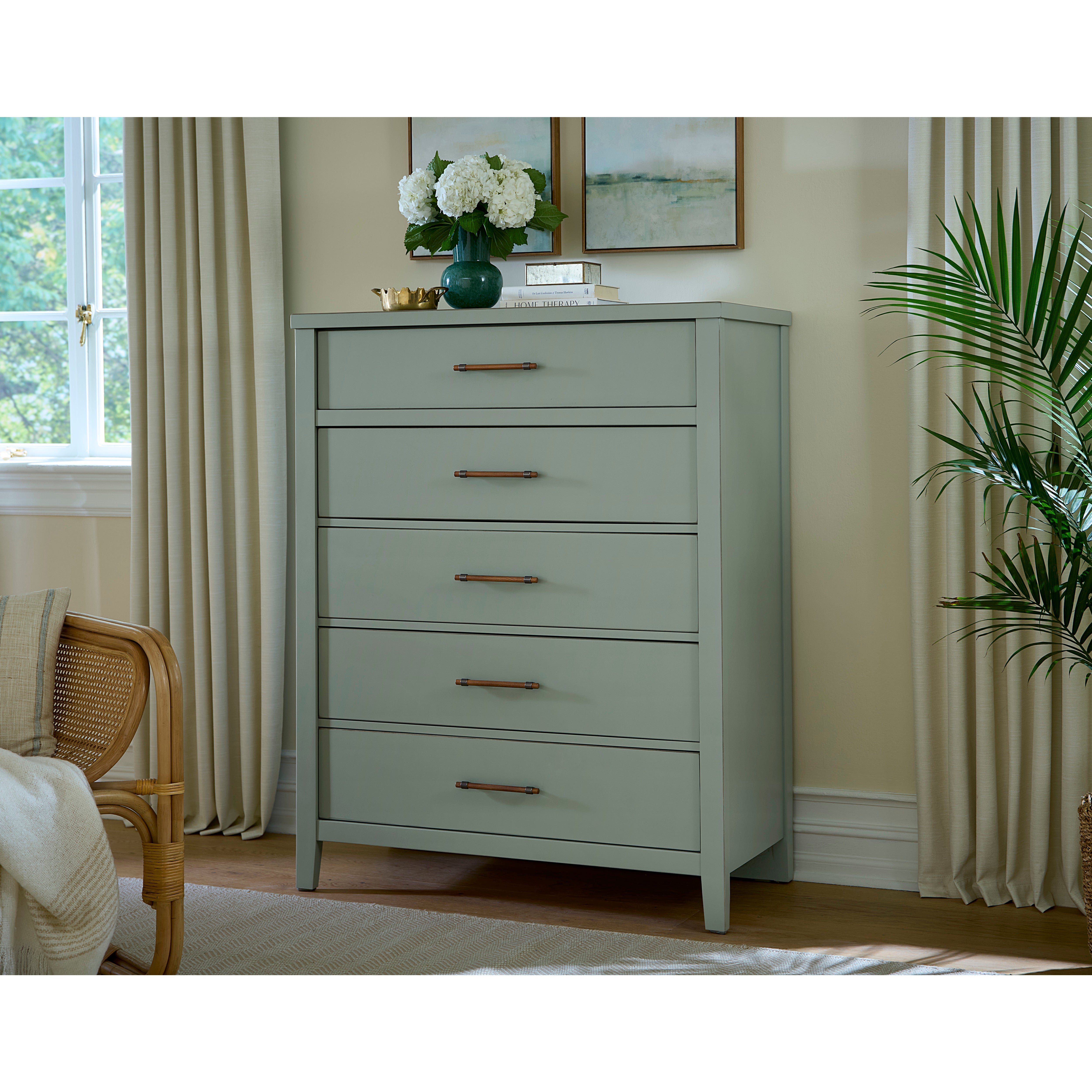 Light green chest of drawers with five handles in a bright, neutral bedroom setting.