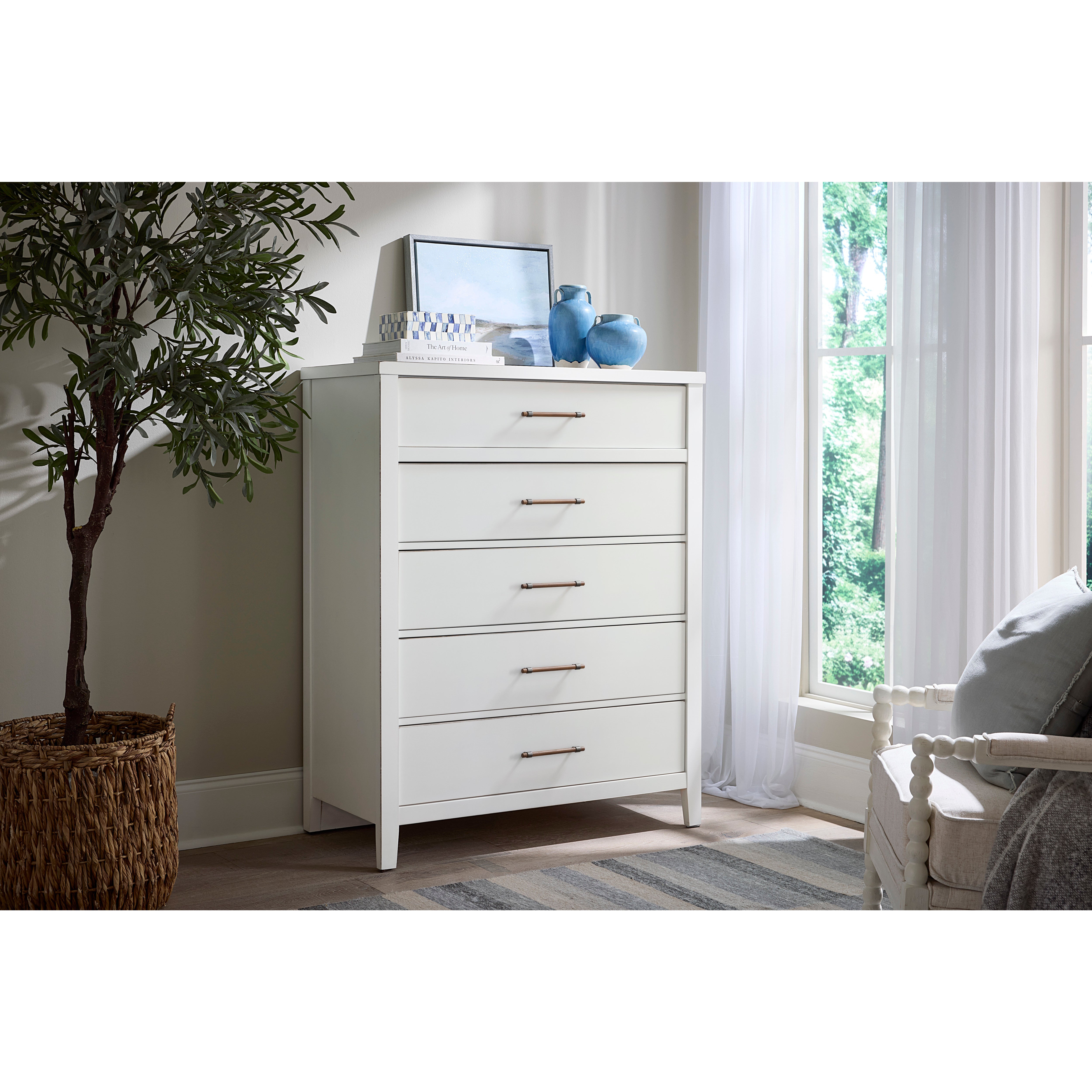 White five-drawer chest with decorative items on top in a bright, modern bedroom.