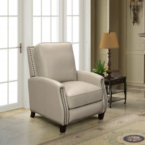 Light gray leather recliner chair in a bright living room next to a side table and lamp.