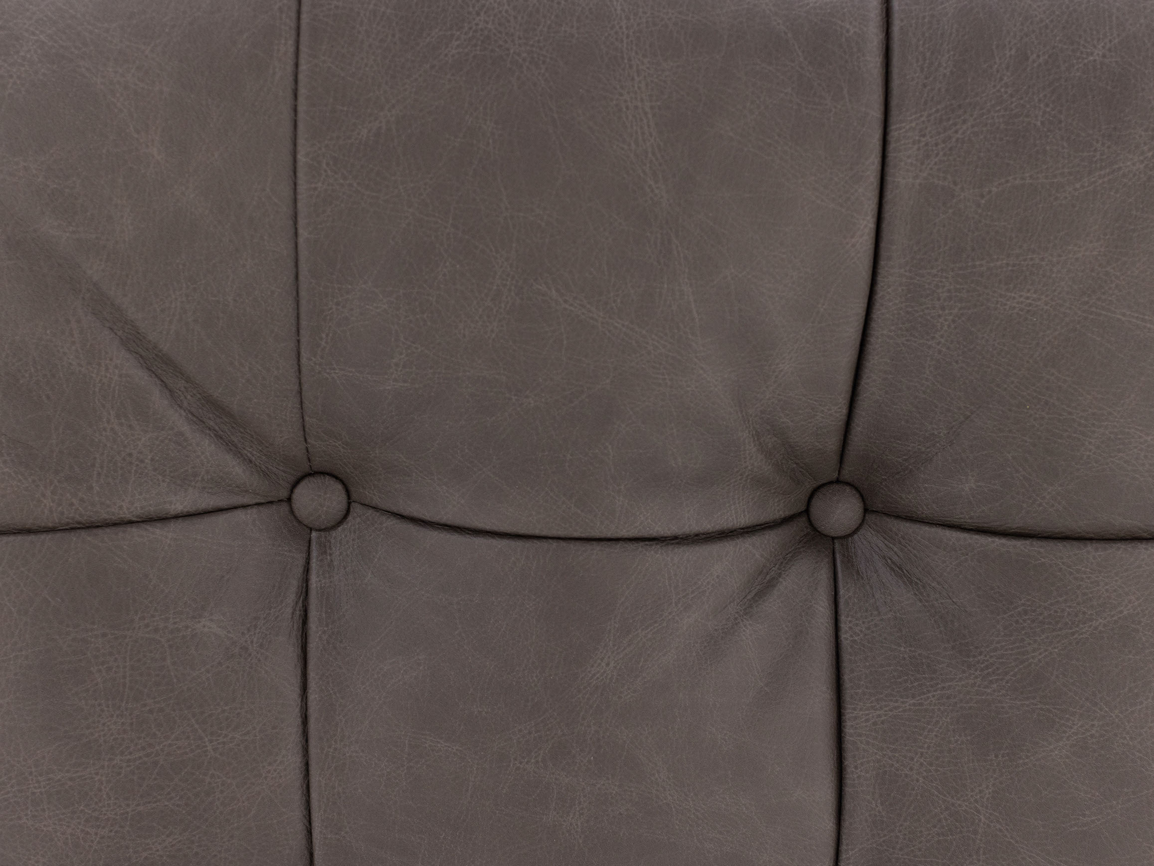 Close-up of tufted dark gray leather upholstery with two buttons.
