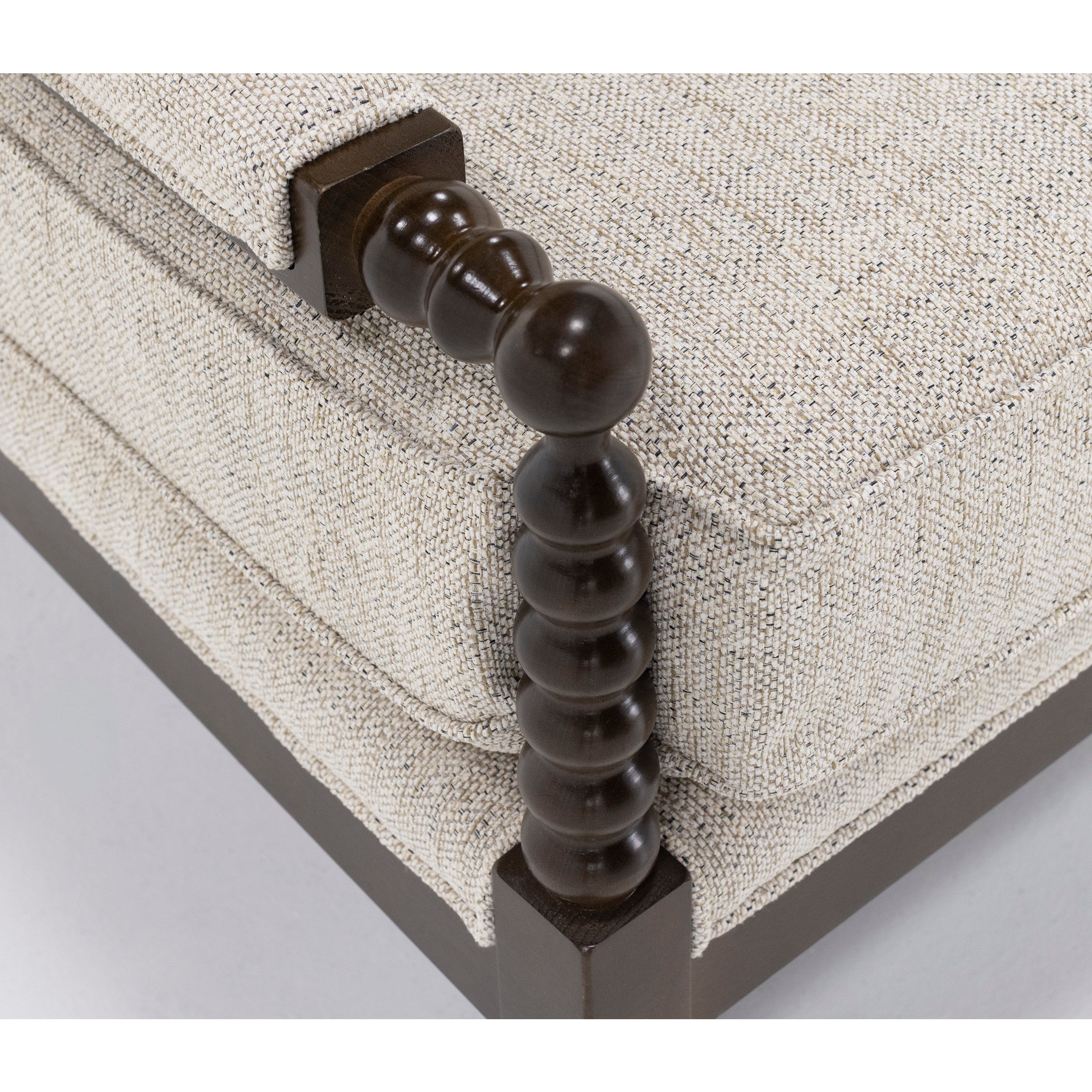 Close-up of a beige upholstered sofa cushion with a dark wood spindle armrest.