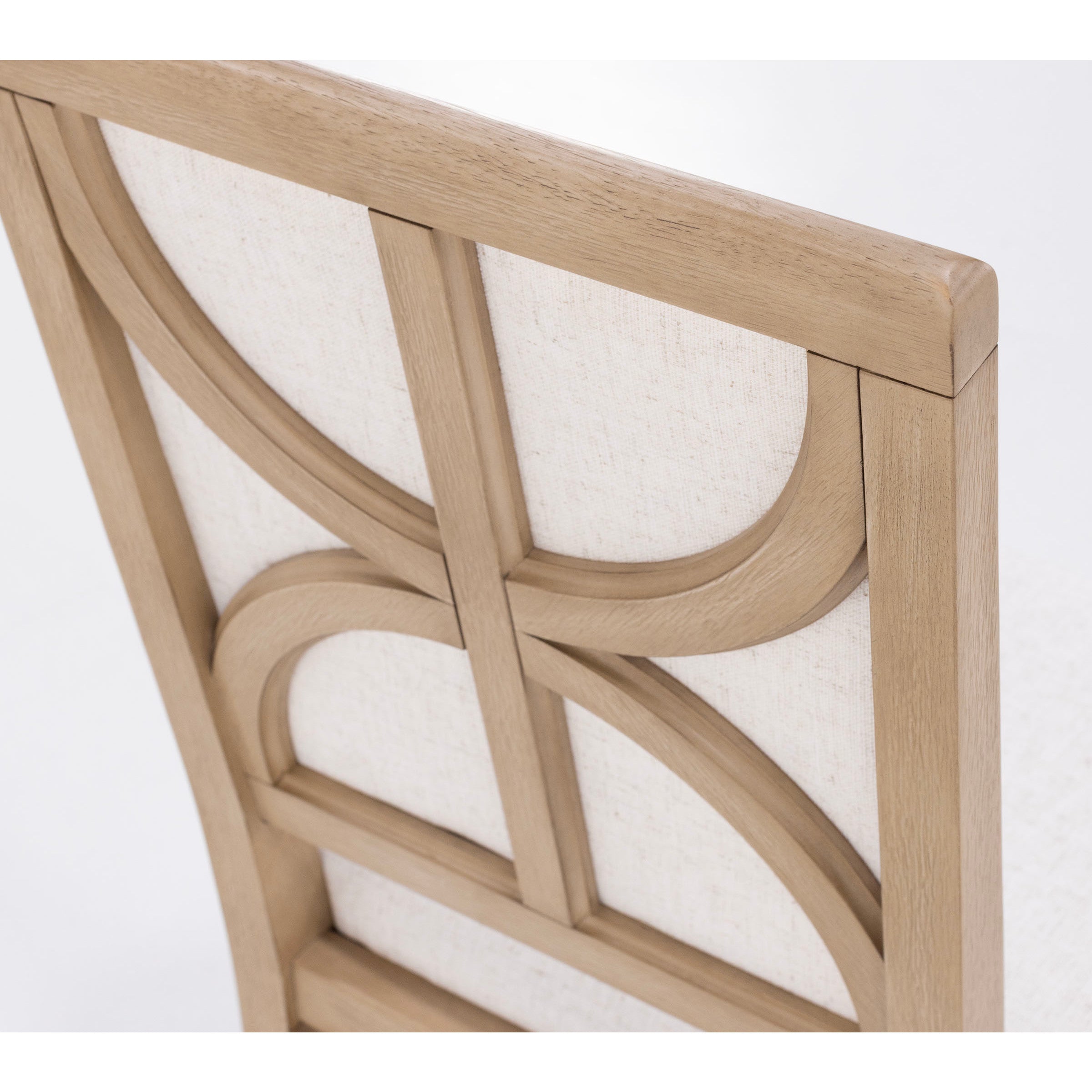 Detail of a wooden chair back with geometric design and light fabric upholstery.
