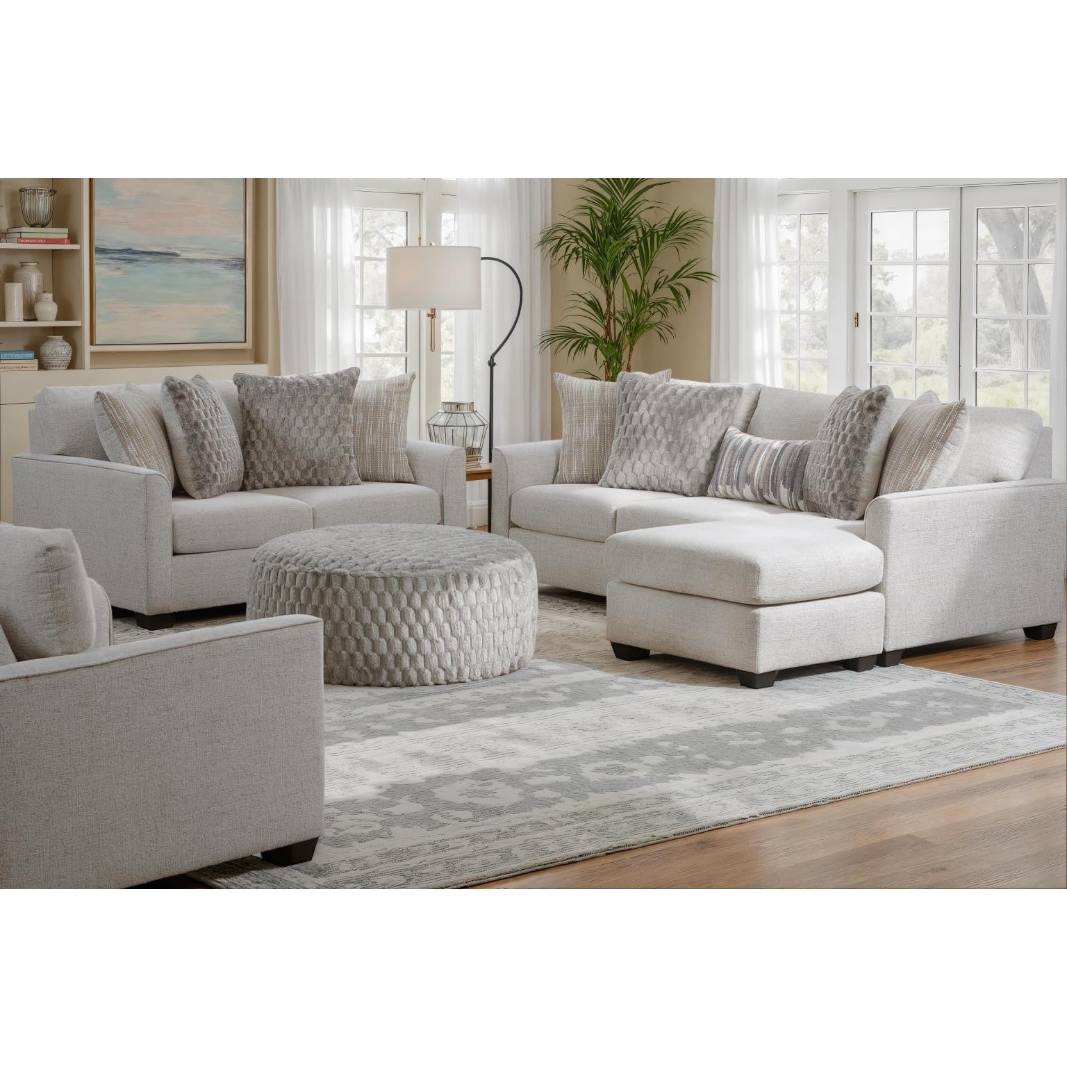 Light gray sectional sofa with chaise, round ottoman, and accent pillows in a bright living room.