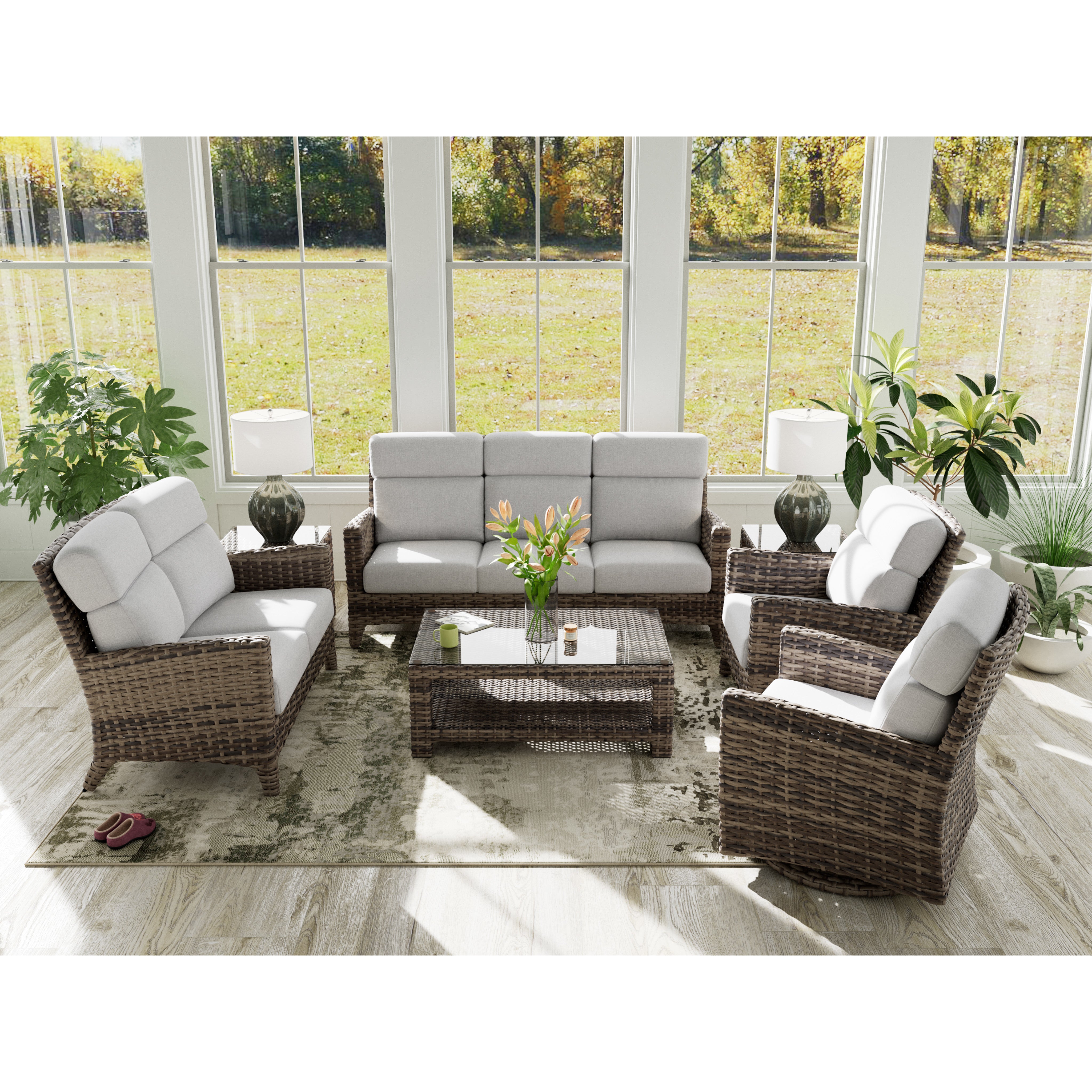 Wicker patio furniture set with light gray cushions in a bright sunroom with large windows.