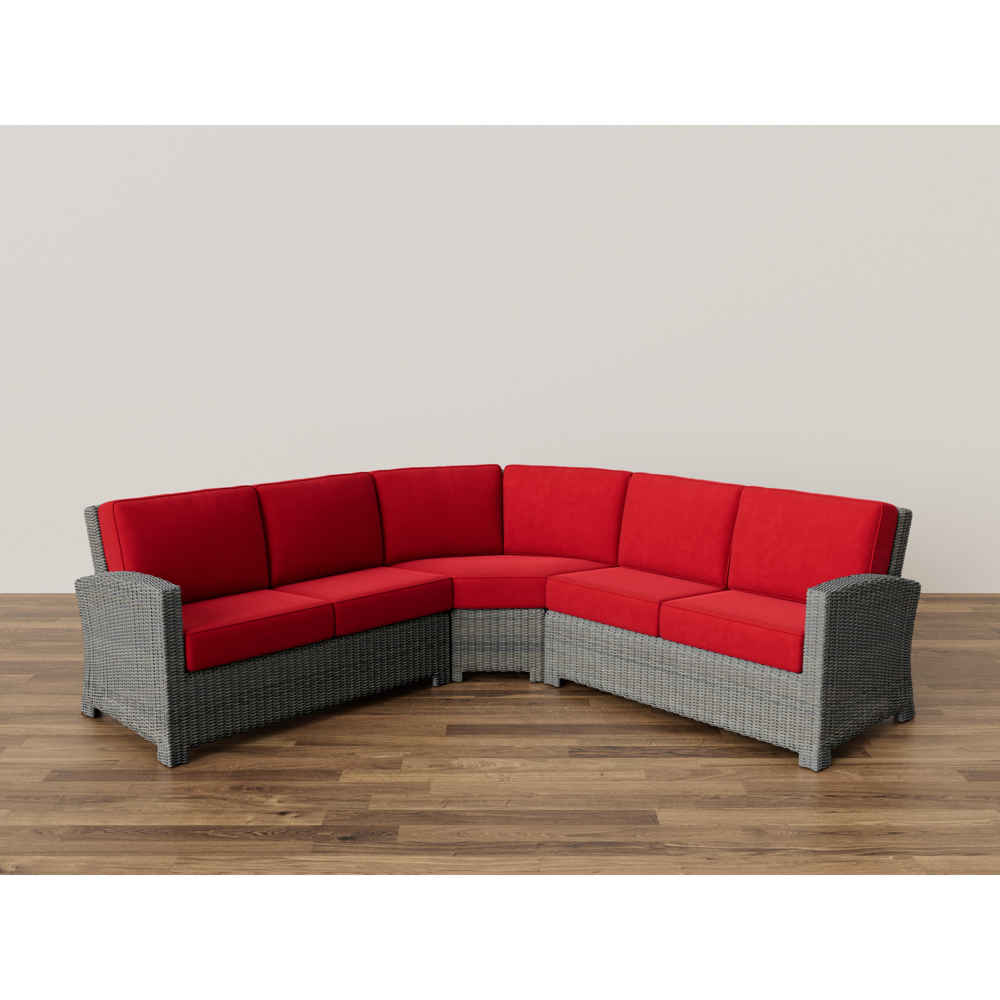 Gray wicker sectional sofa with red cushions on wood floor.