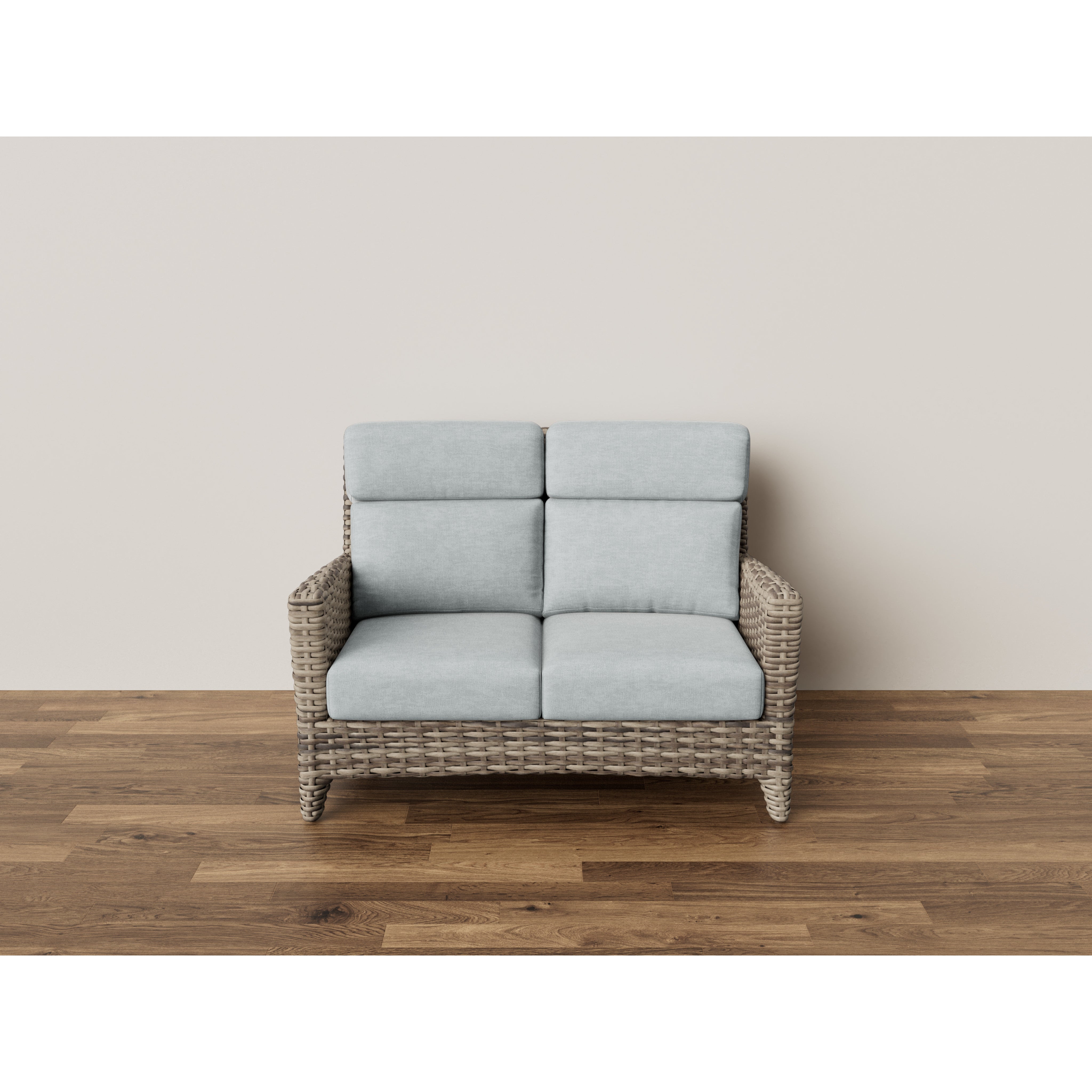 Wicker loveseat with light gray cushions on wooden floor against a plain wall.