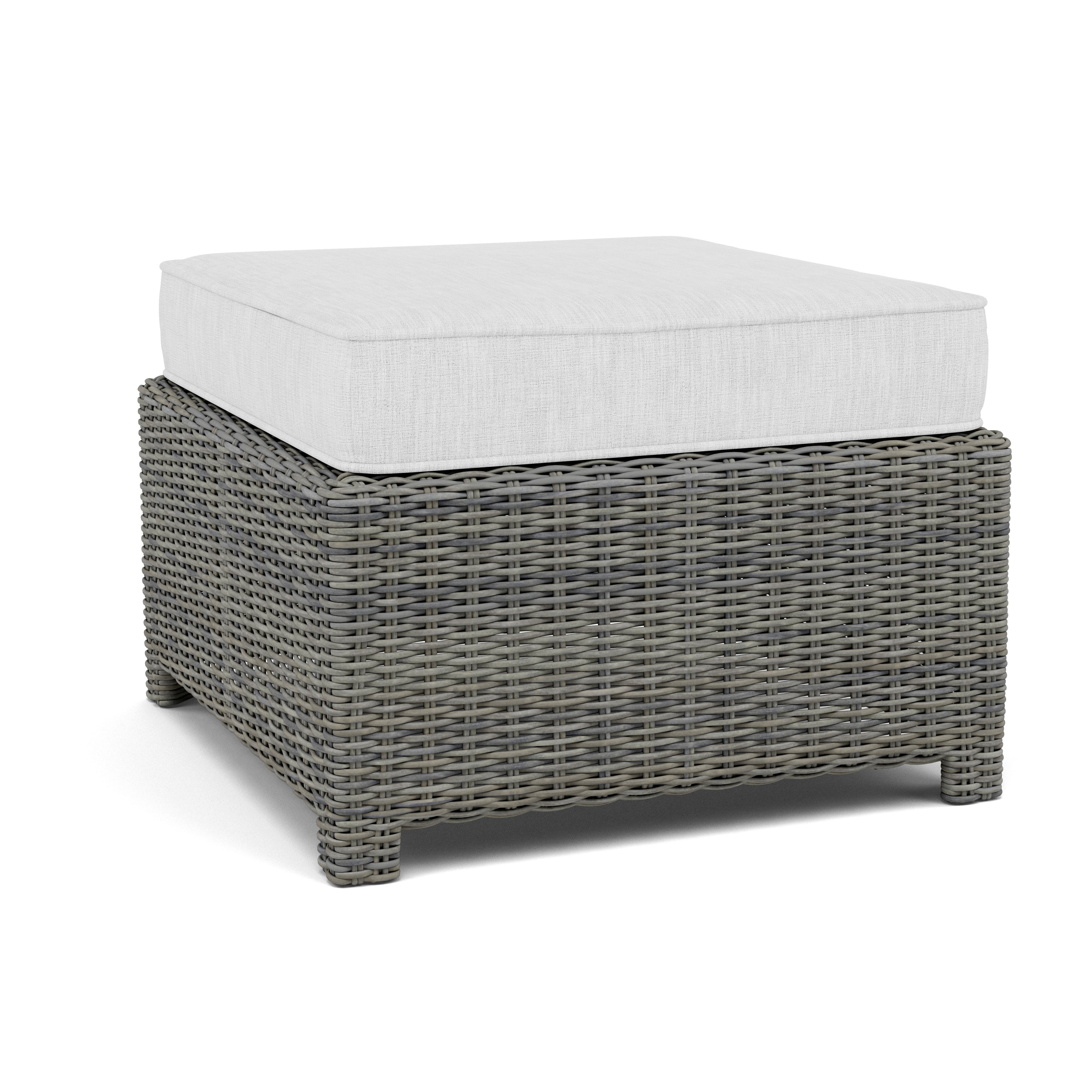 Gray wicker ottoman with a white cushion, suitable for indoor or outdoor seating.