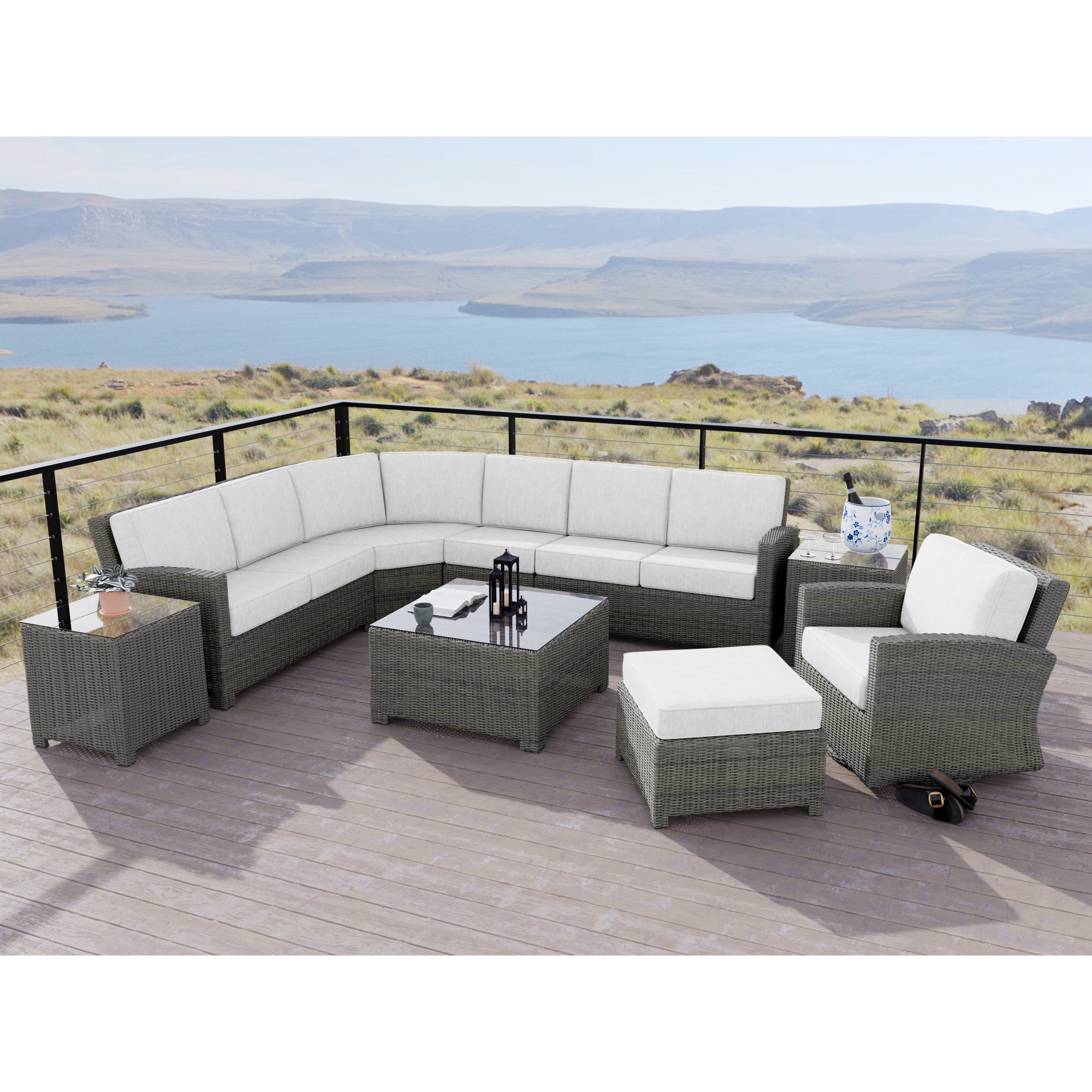 Outdoor patio set with gray wicker furniture, white cushions, and glass table overlooking a lake.