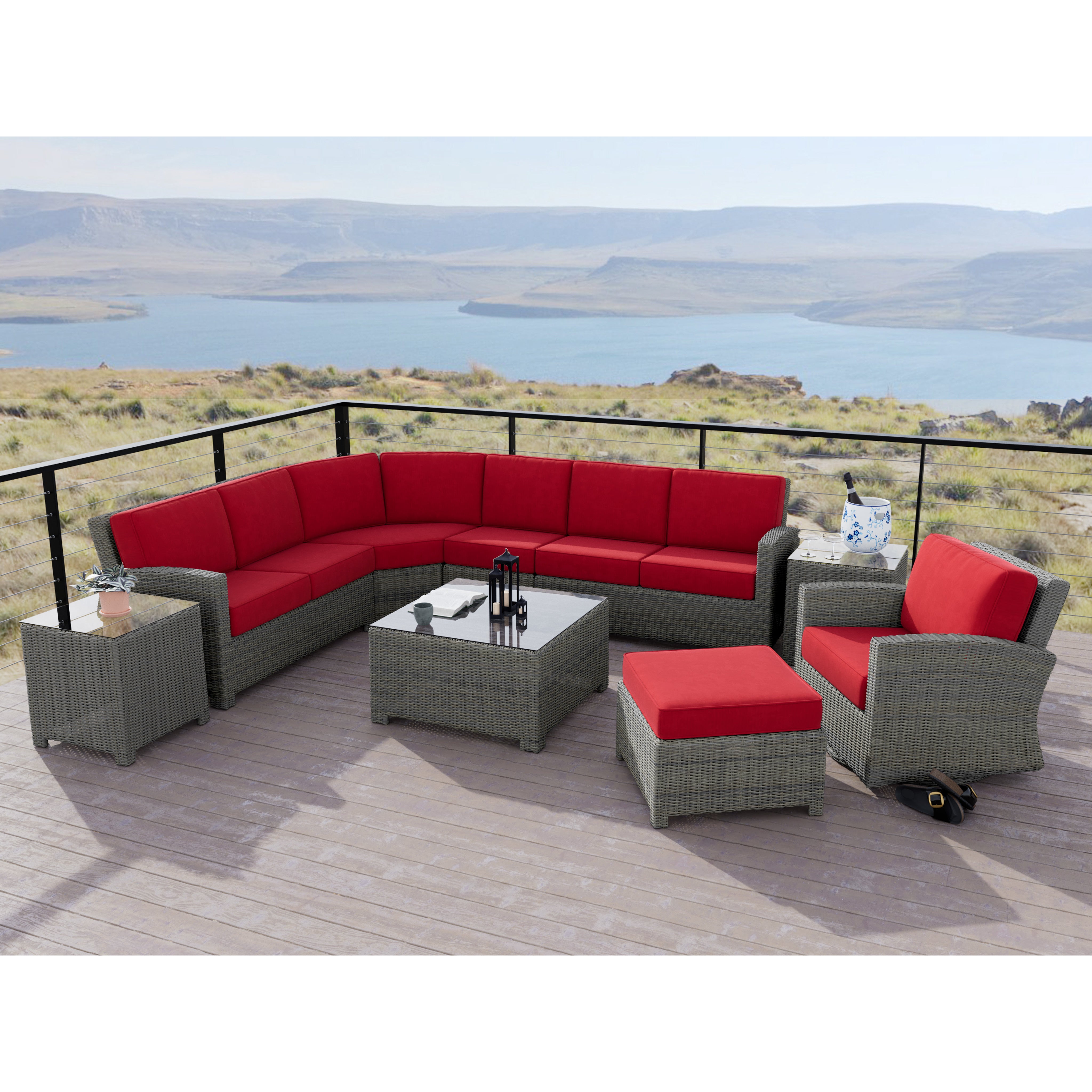 Outdoor patio set with gray wicker furniture and red cushions on a deck overlooking a lake.