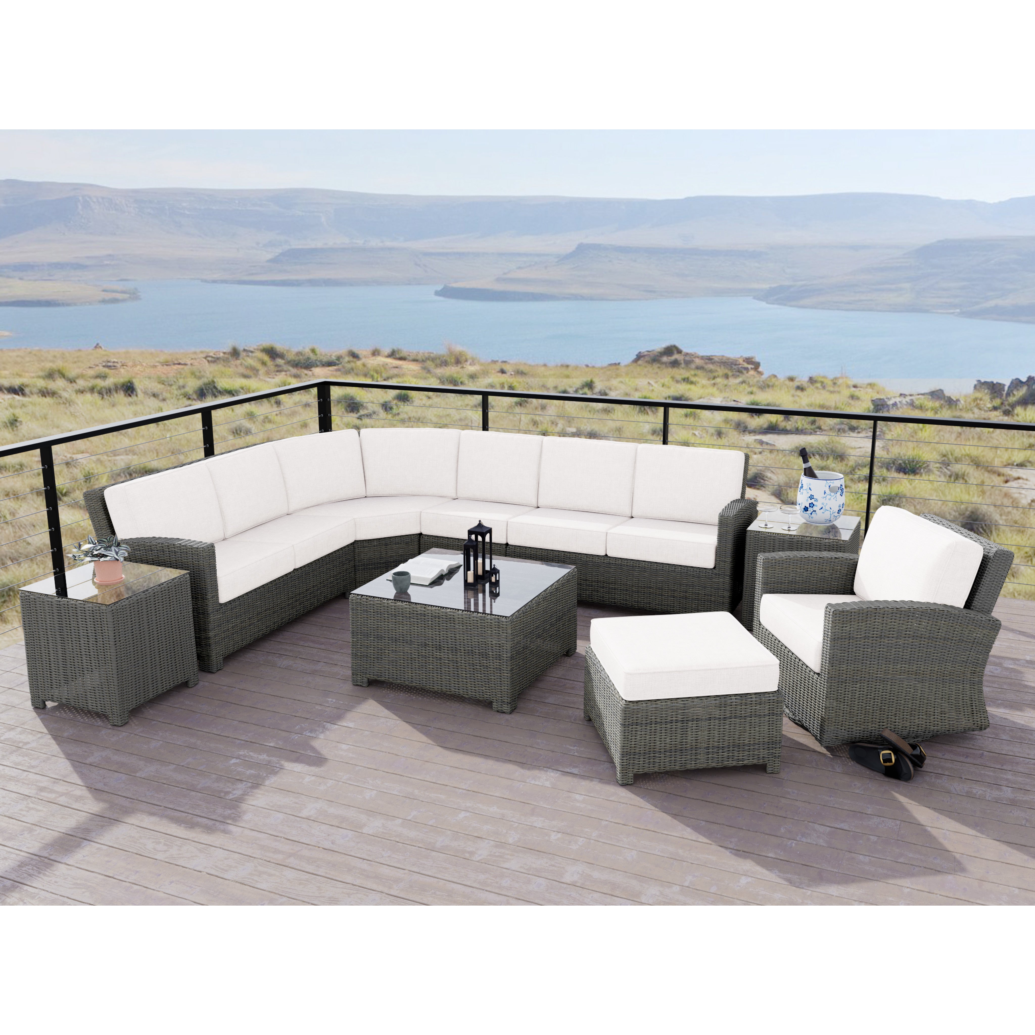 Outdoor patio set with gray wicker frame, white cushions, and a glass table, overlooking a lake.