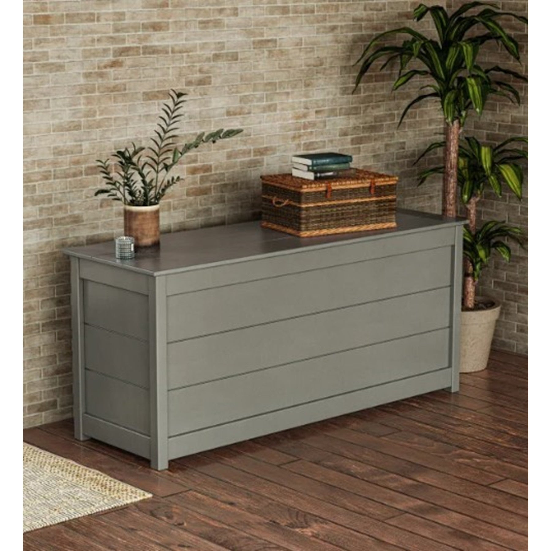 Gray storage bench against brick wall, topped with a plant, wicker basket, and books.