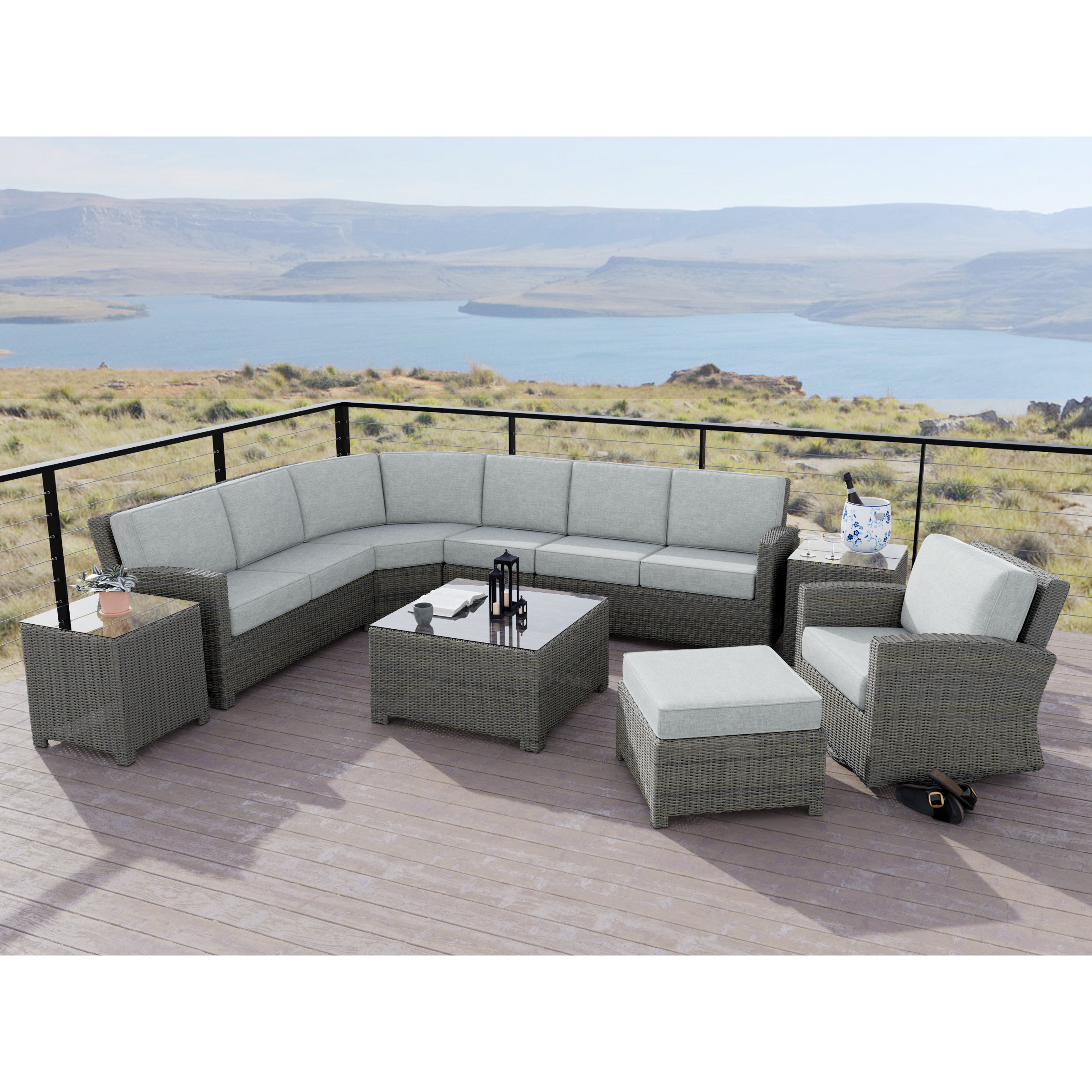 Outdoor sectional patio furniture with glass tables and gray cushions on a deck overlooking water.