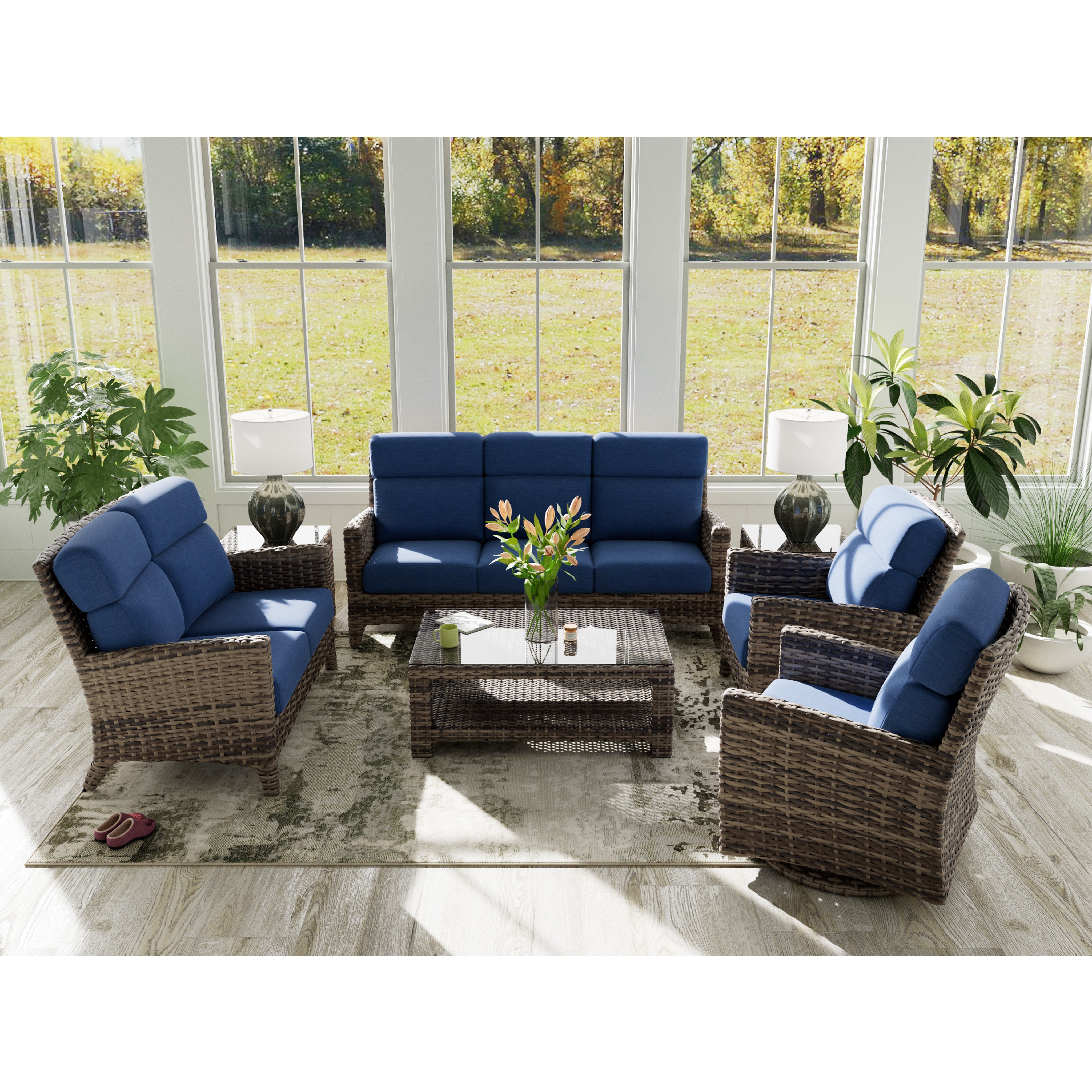 Wicker patio furniture set with blue cushions in a sunroom with large windows and green plants.