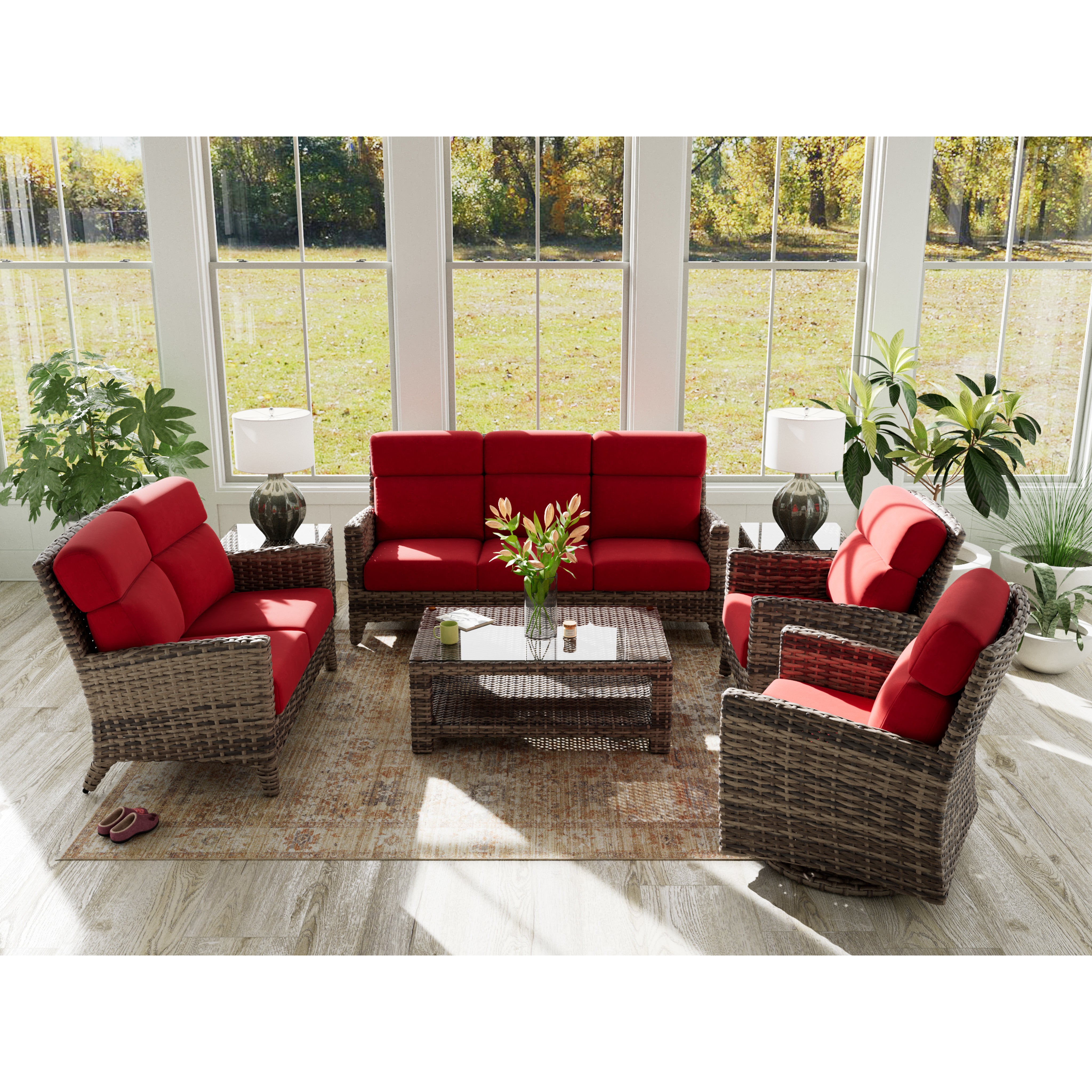 Wicker furniture set with red cushions in a bright sunroom with large windows and indoor plants.