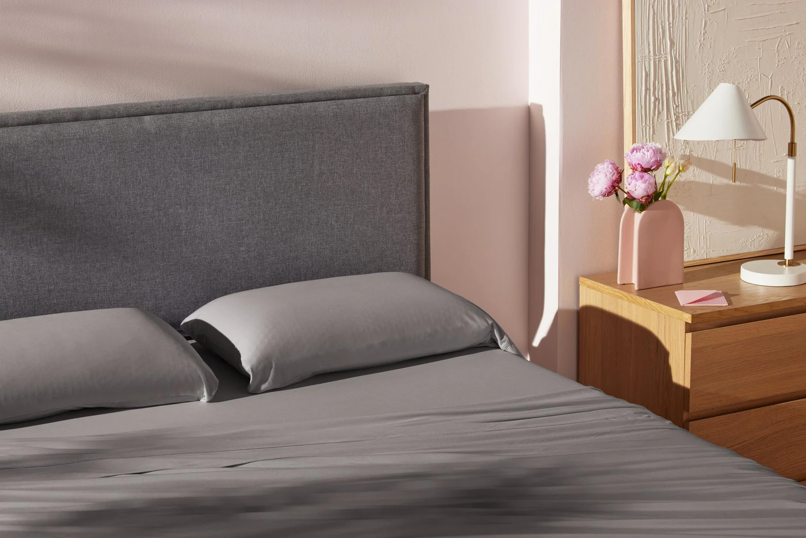 Bedroom with a bed featuring gray bedding and pillows, a nightstand with a lamp and vase.