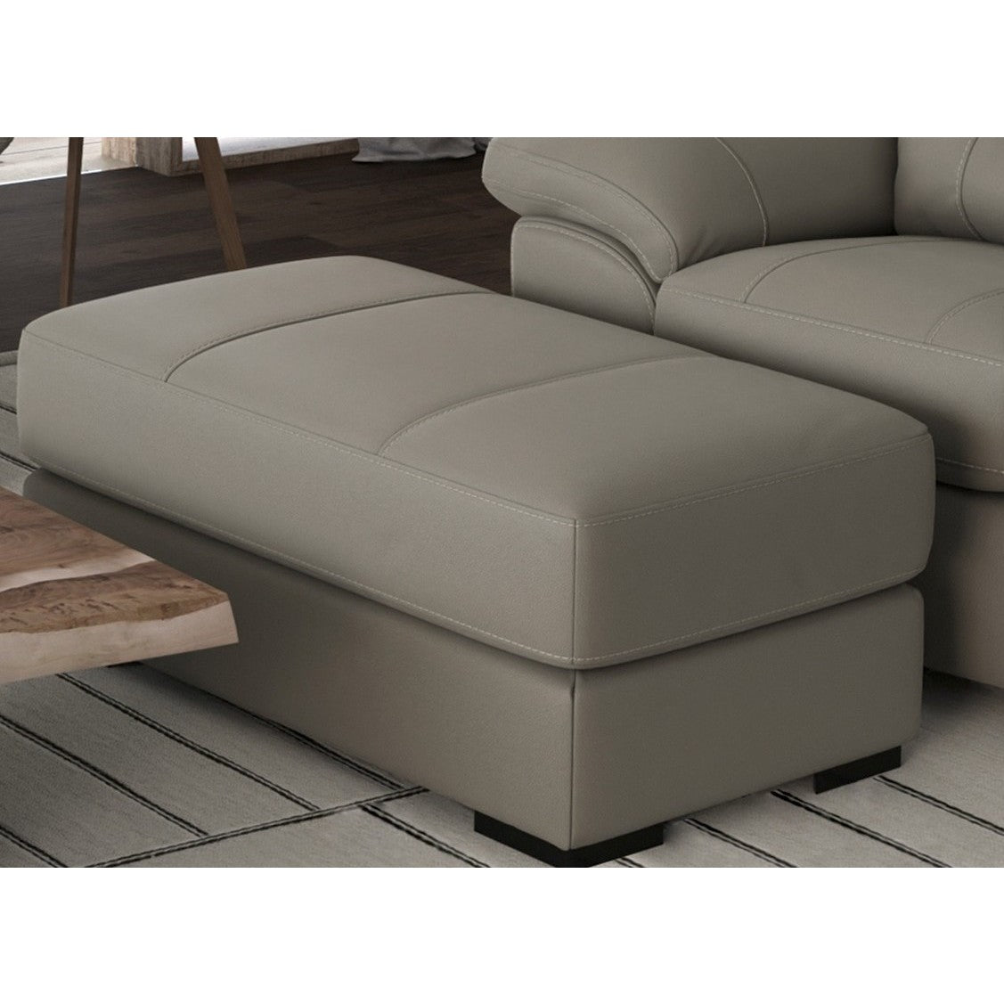 Light gray rectangular ottoman with stitched details, placed on a striped rug next to a sofa.