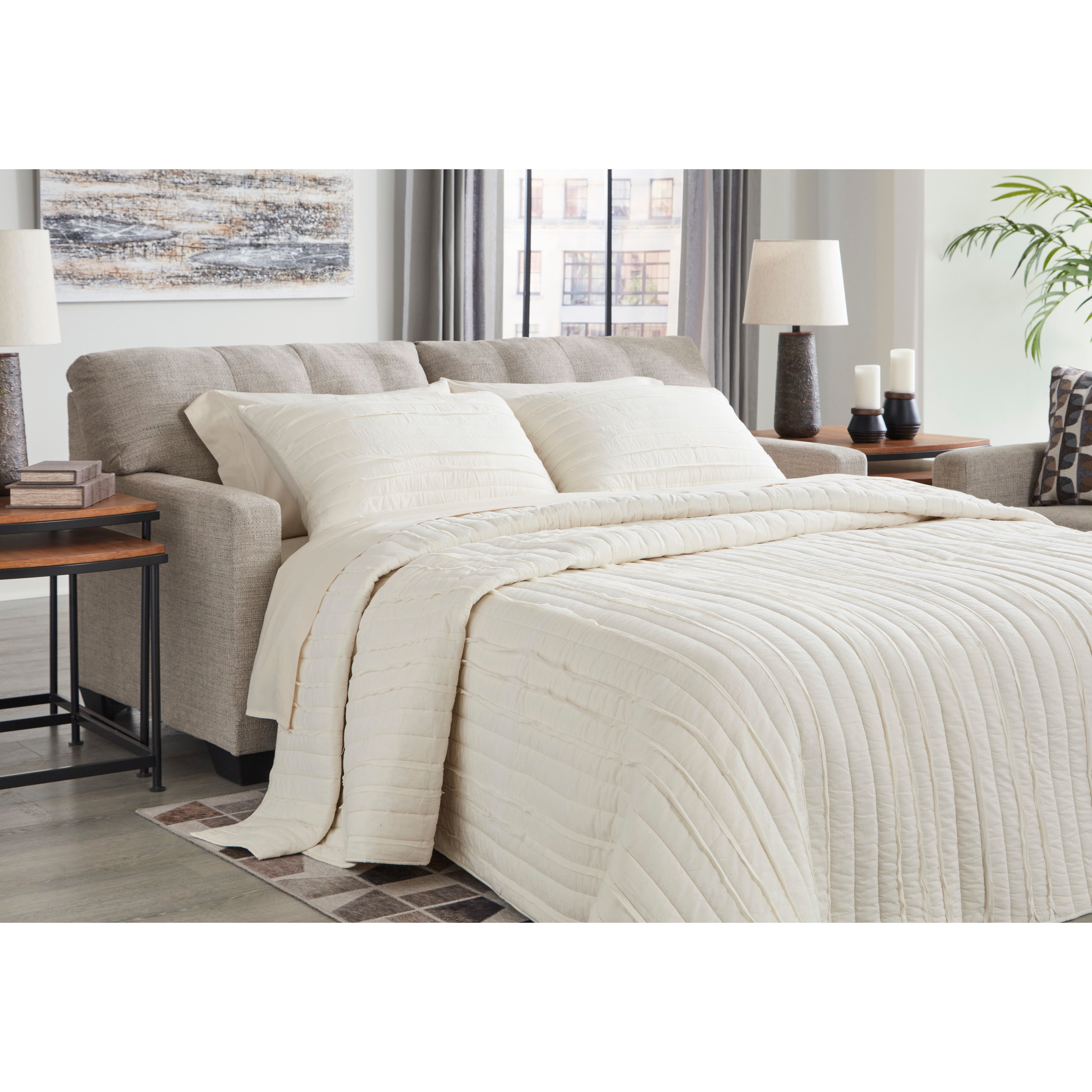 Beige comforter and pillows on sleeper sofa in modern living room.