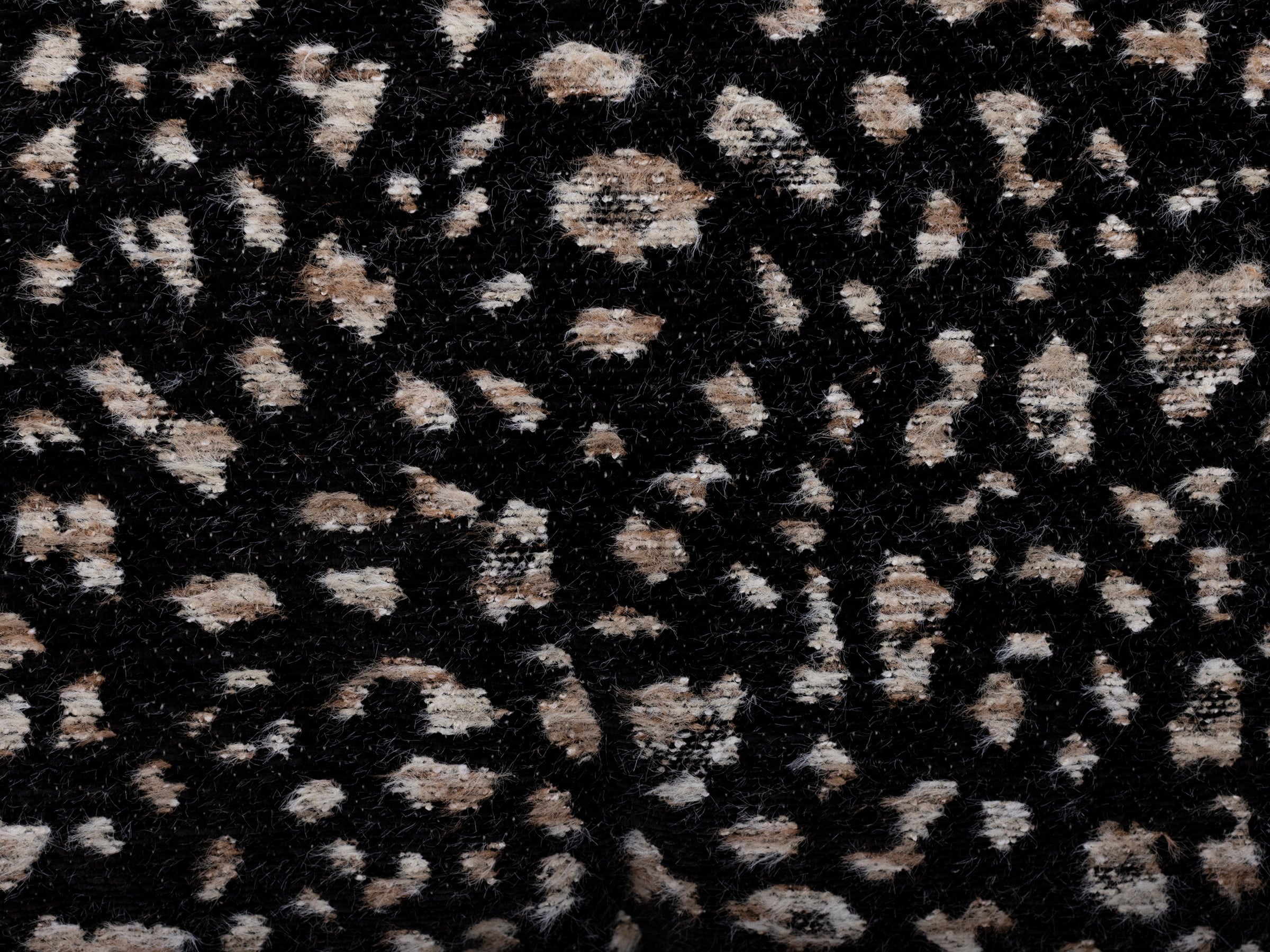 Close-up of black fabric with a tan and white animal print pattern.